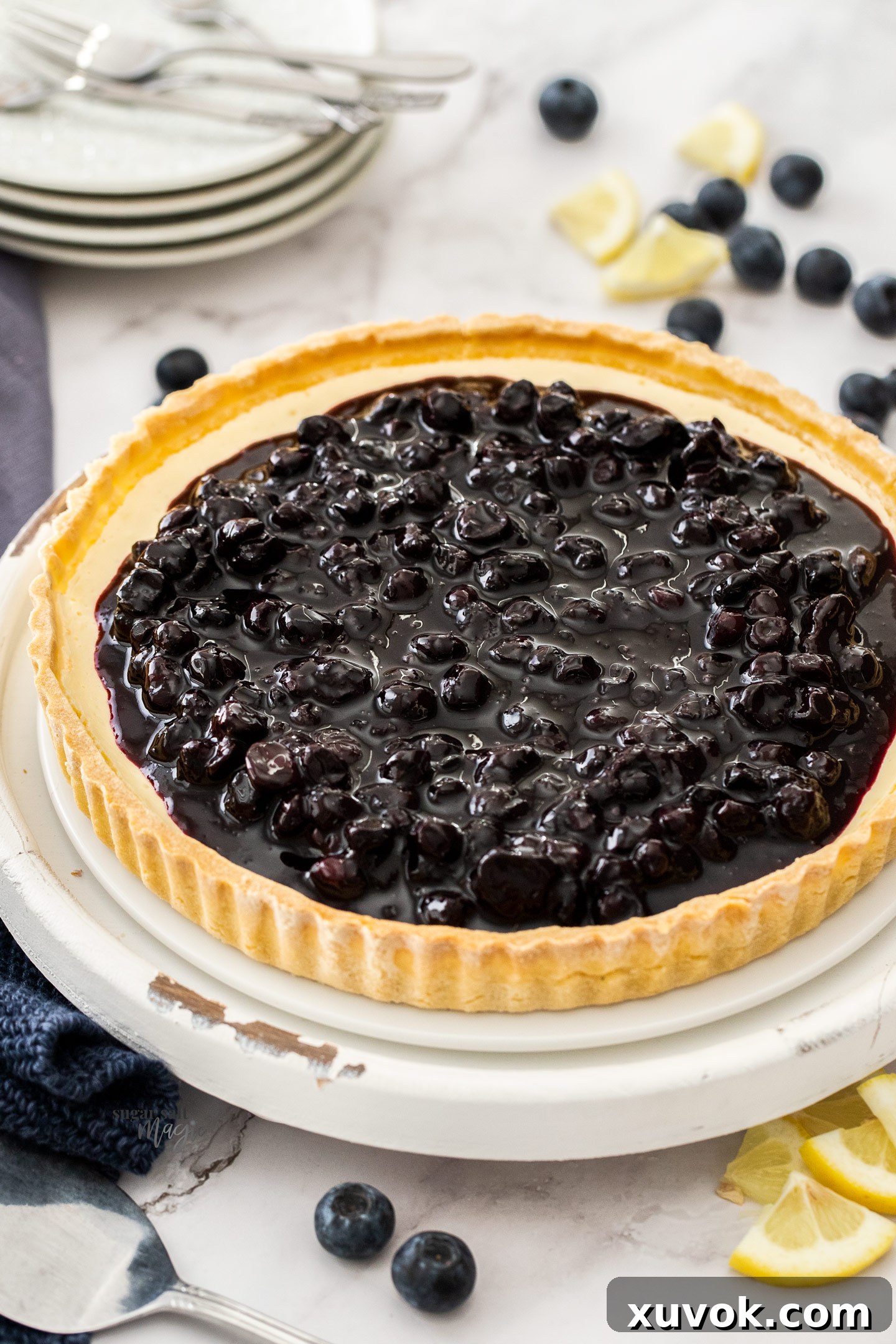 A complete blueberry cheese tart, richly topped with glossy blueberry compote and adorned with fresh blueberries, resting on a white platter.