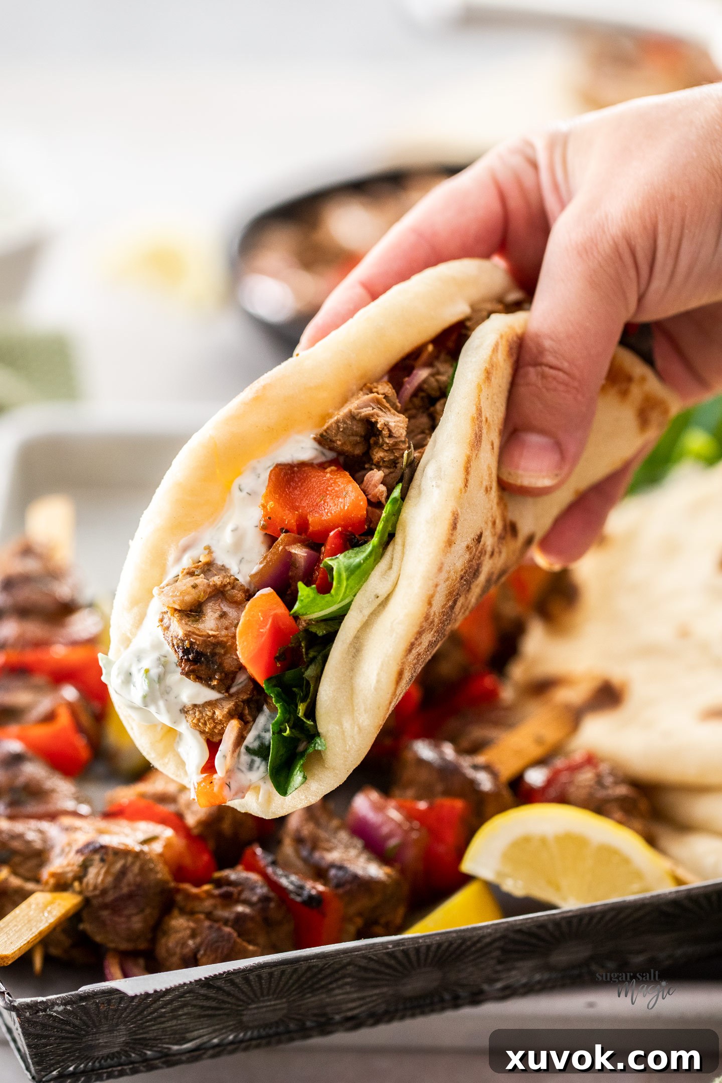 A hand holding a Greek lamb wrap, showcasing the delicious filling.