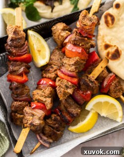 5 Greek lamb kebabs on a dark tray.
