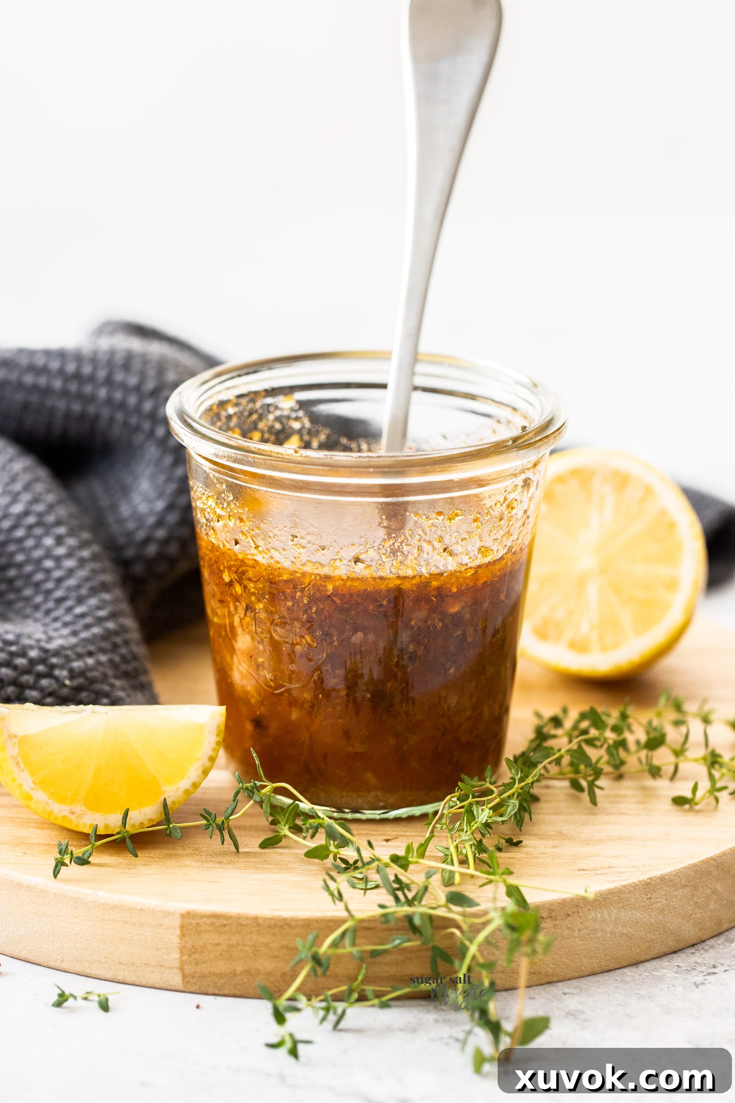 A small glass jar filled with vibrant Greek marinade, surrounded by fresh lemons and thyme sprigs, showcasing its rich texture and natural ingredients.