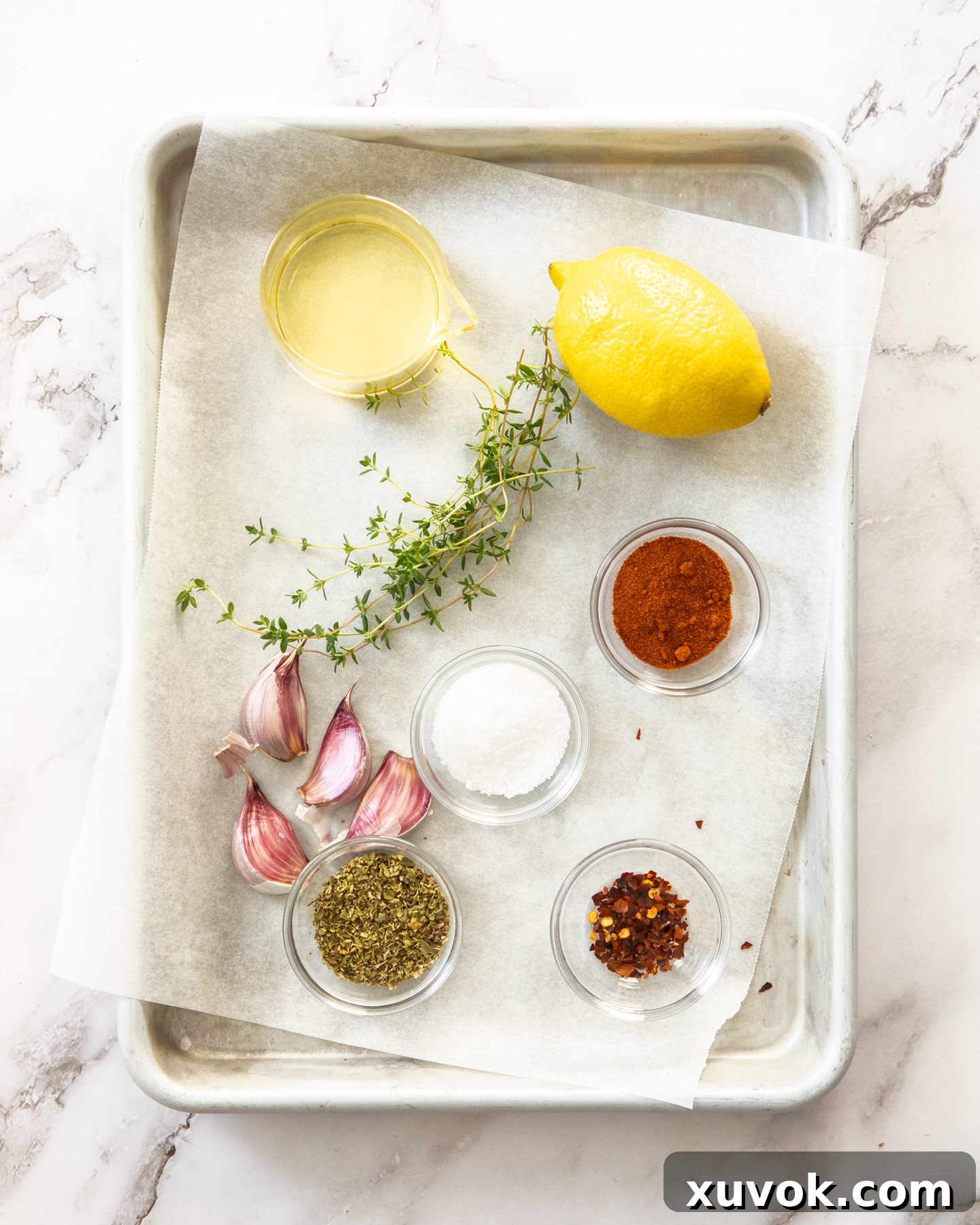 A collection of fresh ingredients for Greek marinade, including lemons, garlic, thyme, and spices, neatly arranged on a baking tray.