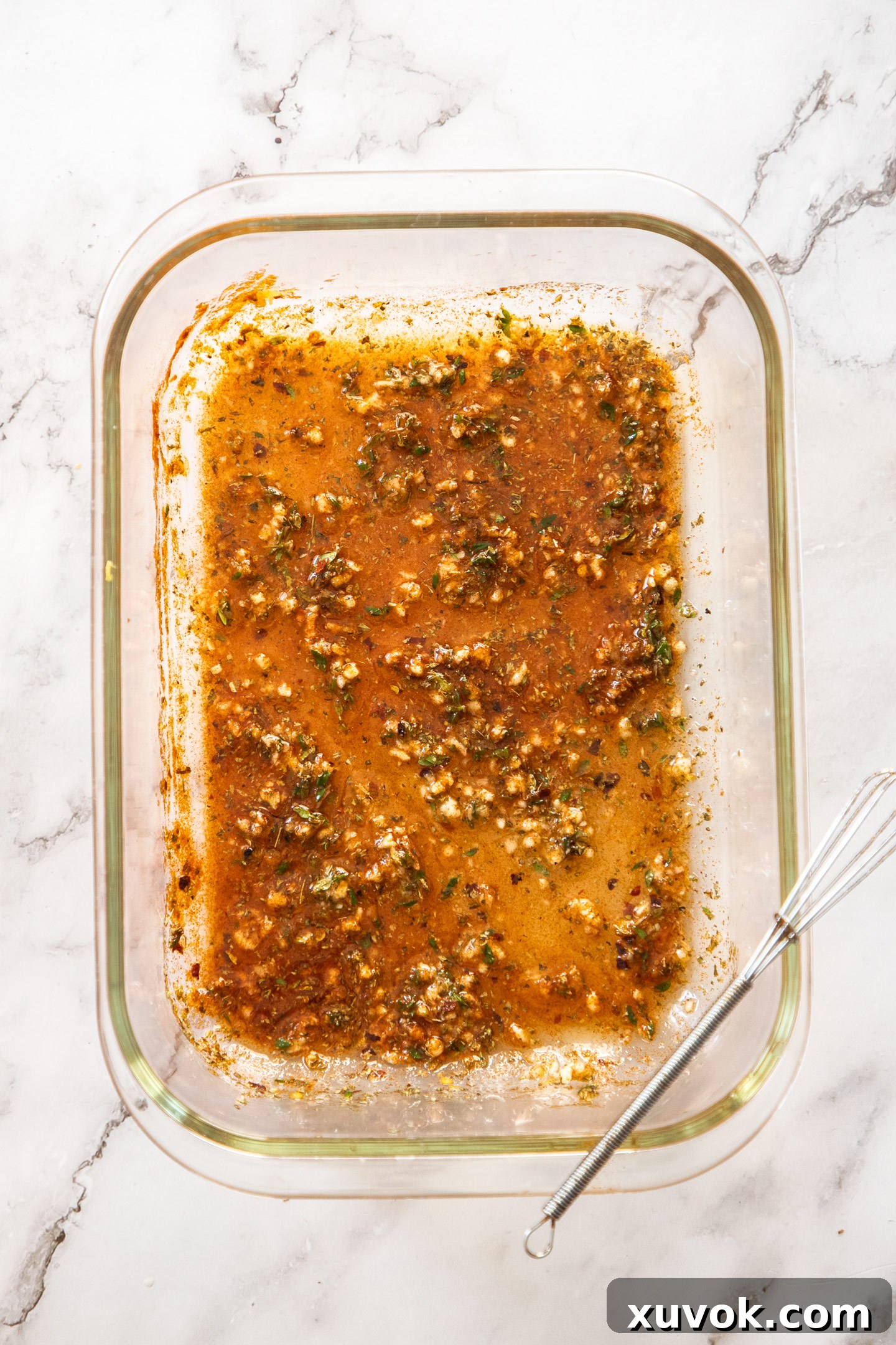 The Greek marinade ingredients, including finely minced garlic, stripped thyme leaves, olive oil, lemon juice, and various spices, are thoroughly mixed together in a large bowl.