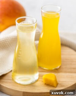 Closeup of two glass bottles of mango syrup on a wooden board.