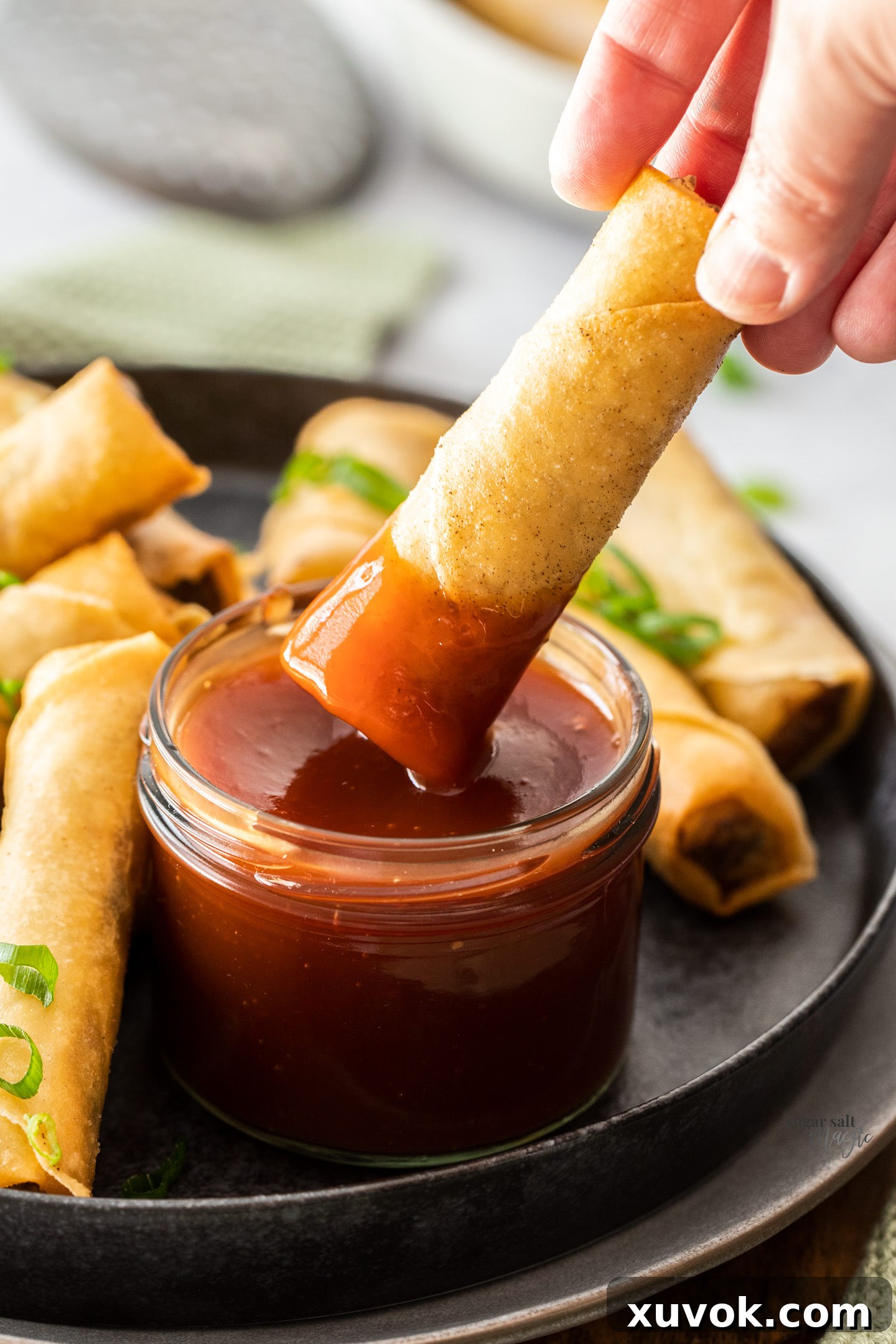 A golden-fried Chinese spring roll being dipped into sweet and sour sauce, showcasing its crisp texture.