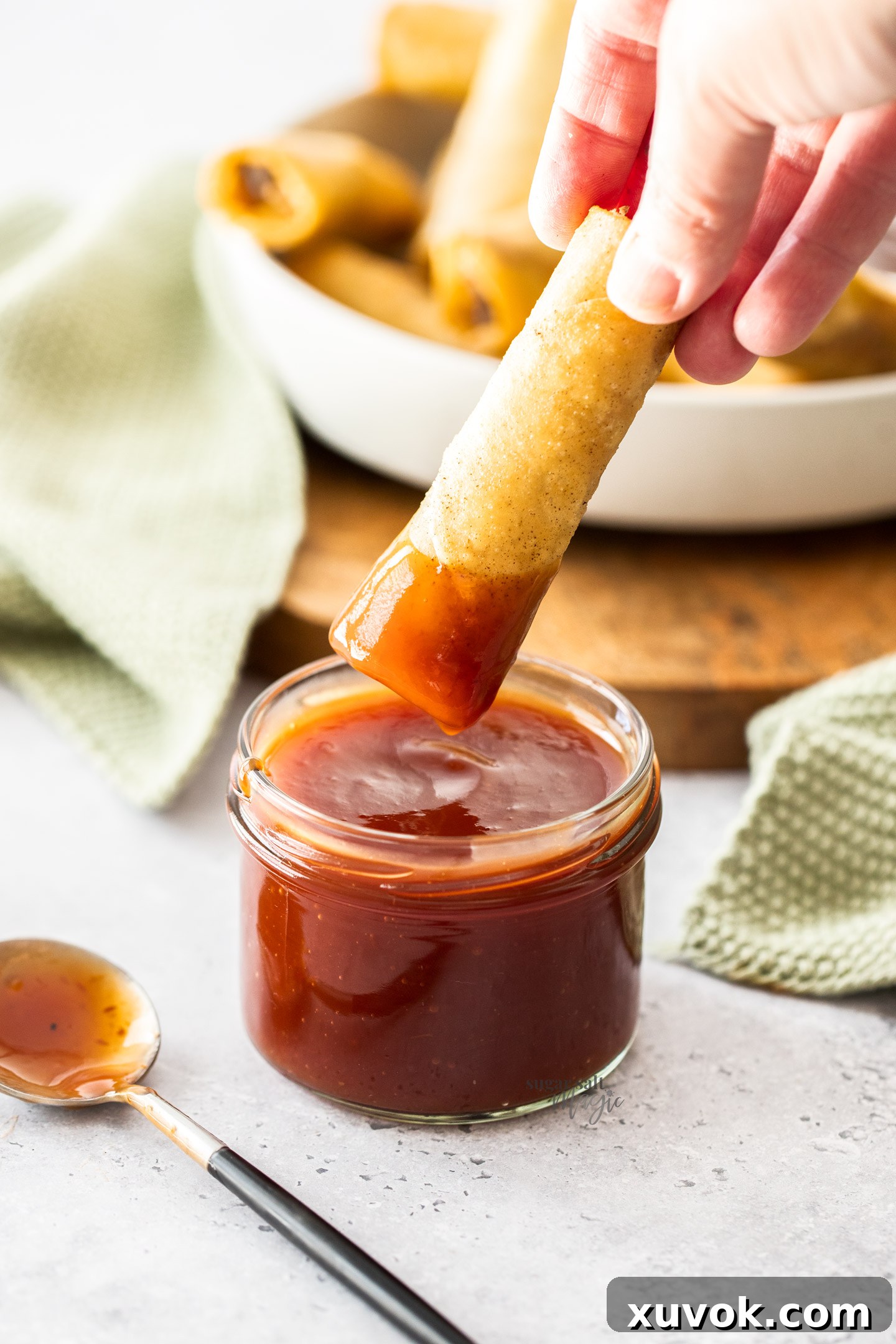A spring roll being dipped into vibrant homemade sweet and sour sauce.