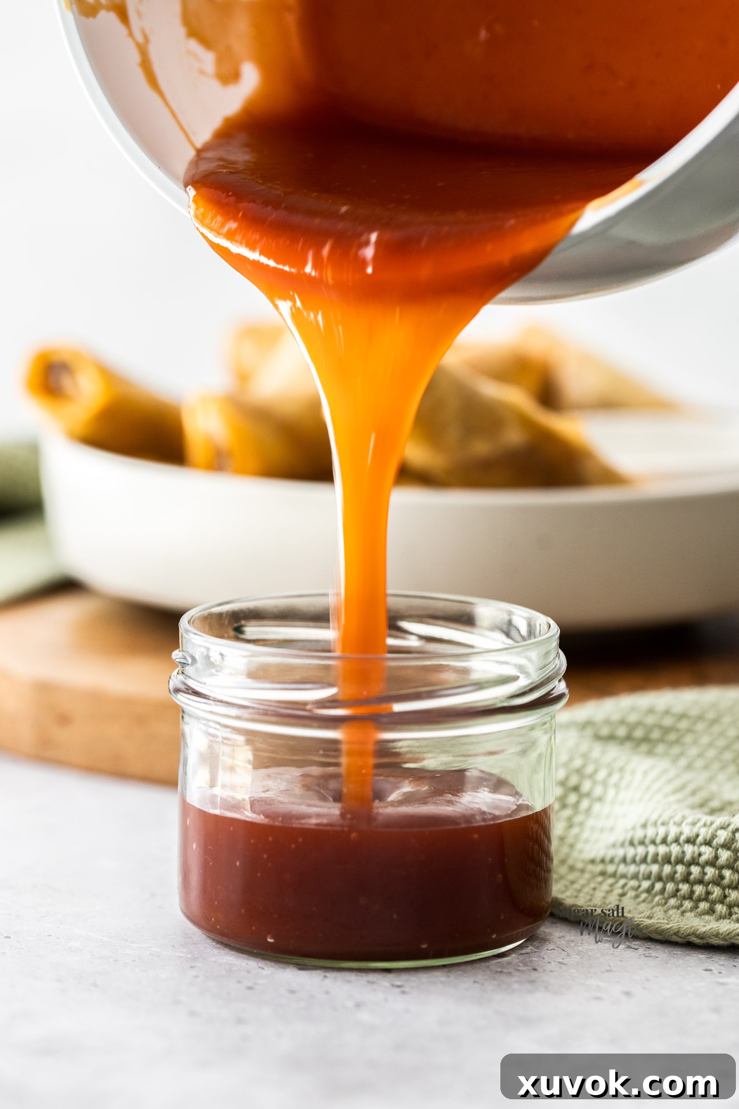 Homemade sweet and sour sauce being poured from a saucepan into a glass jar for storage.