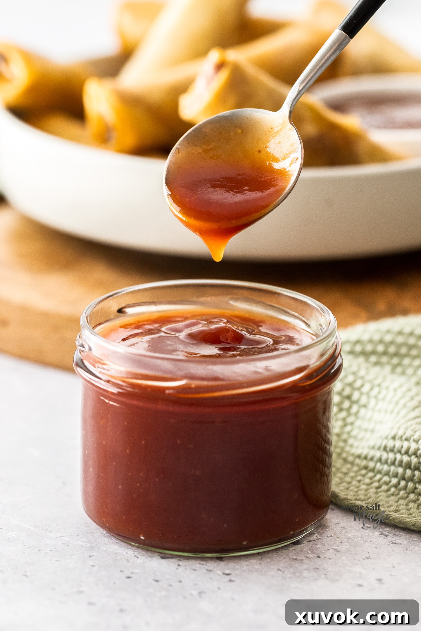 A spoon taking a scoop of homemade sweet and sour sauce from a glass jar.