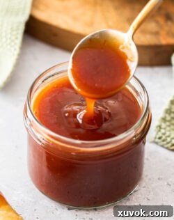 A spoon coming out of a jar with sweet and sour sauce.