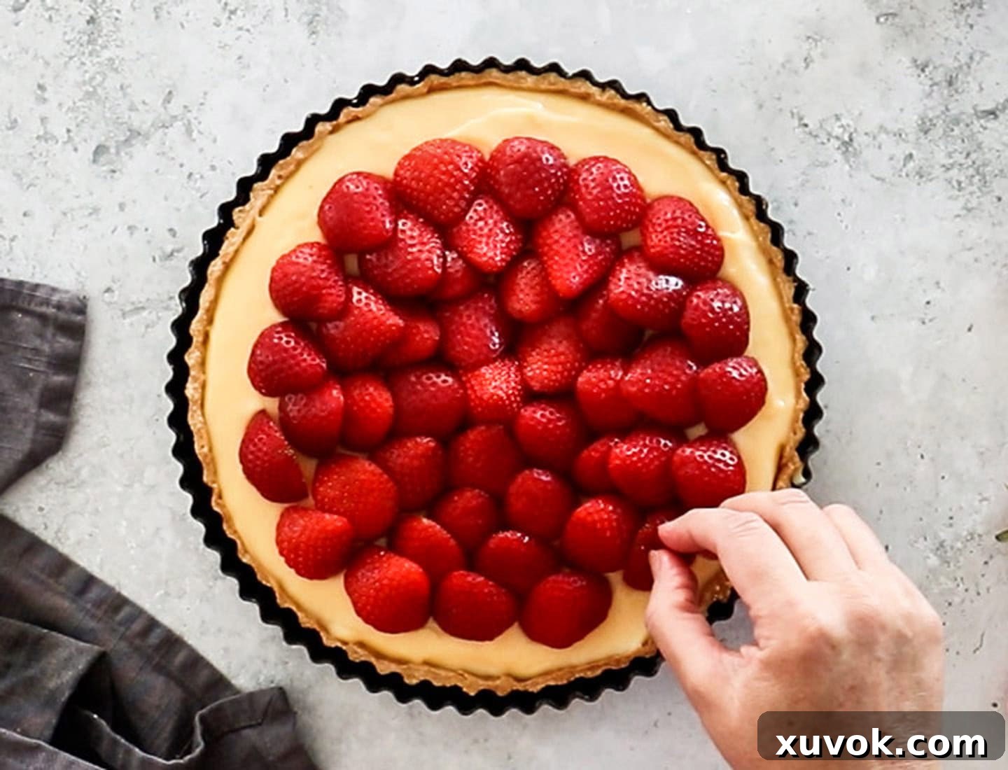 A hand arranging strawberries on the top of the tart.