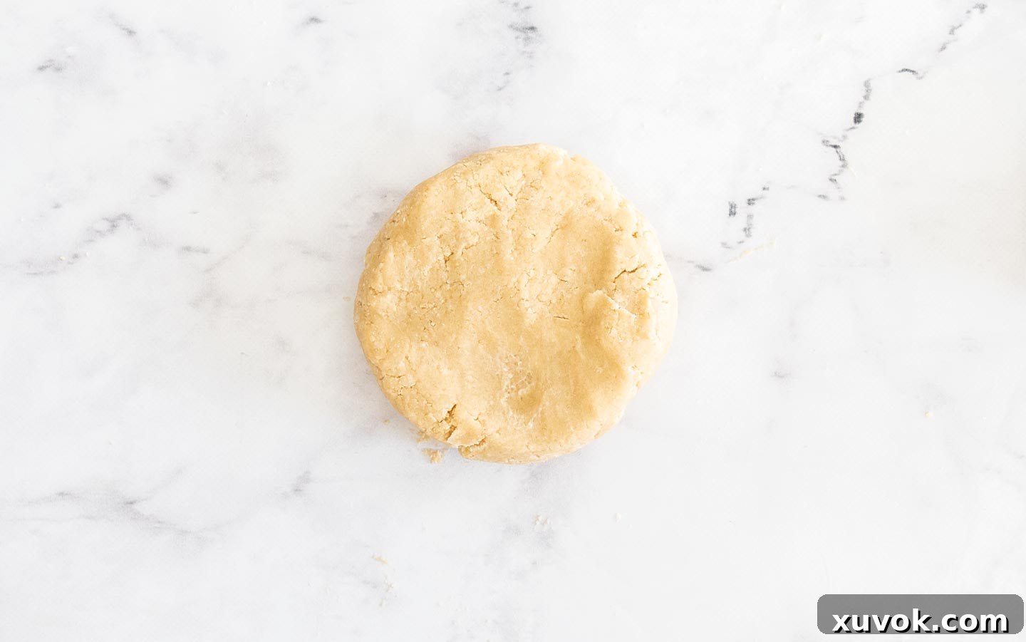 A disk of pastry dough on a marble surface.