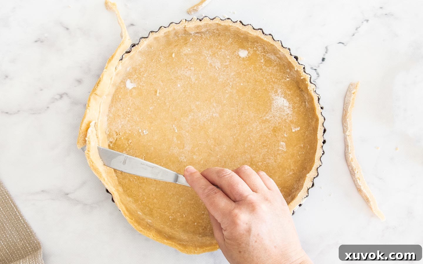 A hand holding a knife slicing away the overhanging pastry.