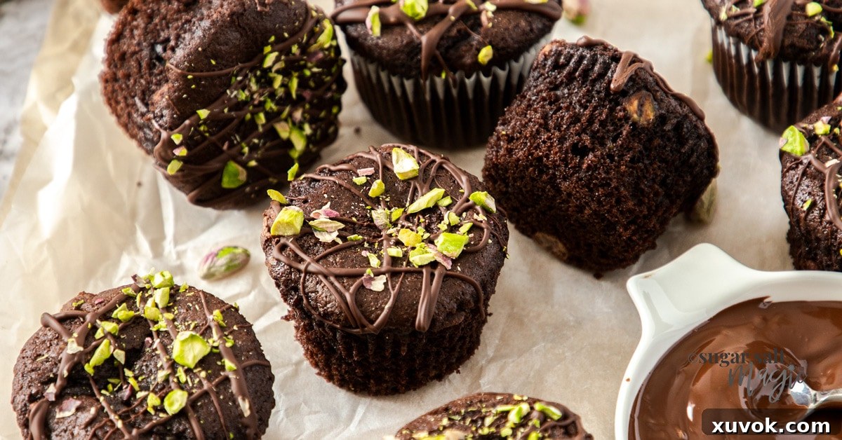 An inviting overhead shot of a batch of freshly baked chocolate pistachio muffins arranged artfully. Each muffin is generously drizzled with melted chocolate and garnished with bright green chopped pistachios, ready to be served.