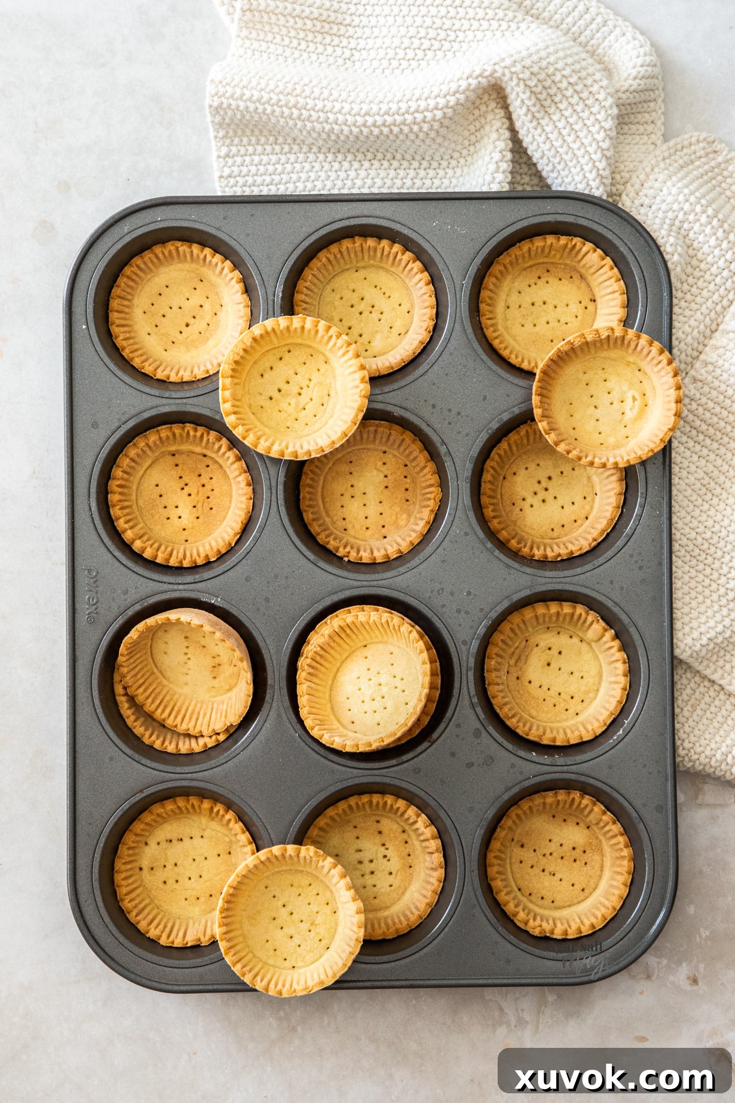 A batch of tartlet shells in a muffin tin, showcasing their golden-brown color and perfect shape.