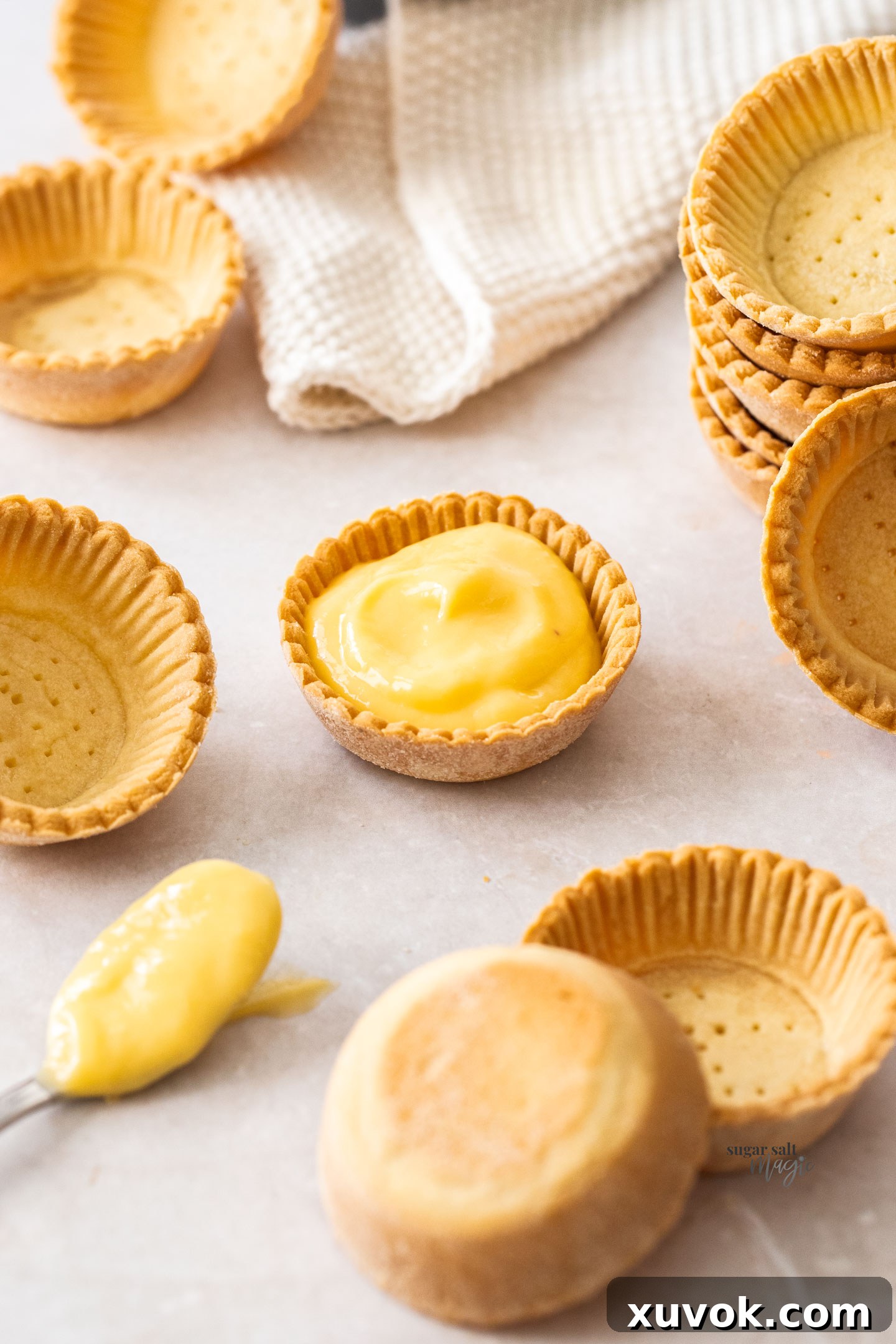 A single tartlet shell filled with vibrant yellow mango curd, garnished with fresh mint, highlighting the crisp edge of the pastry.