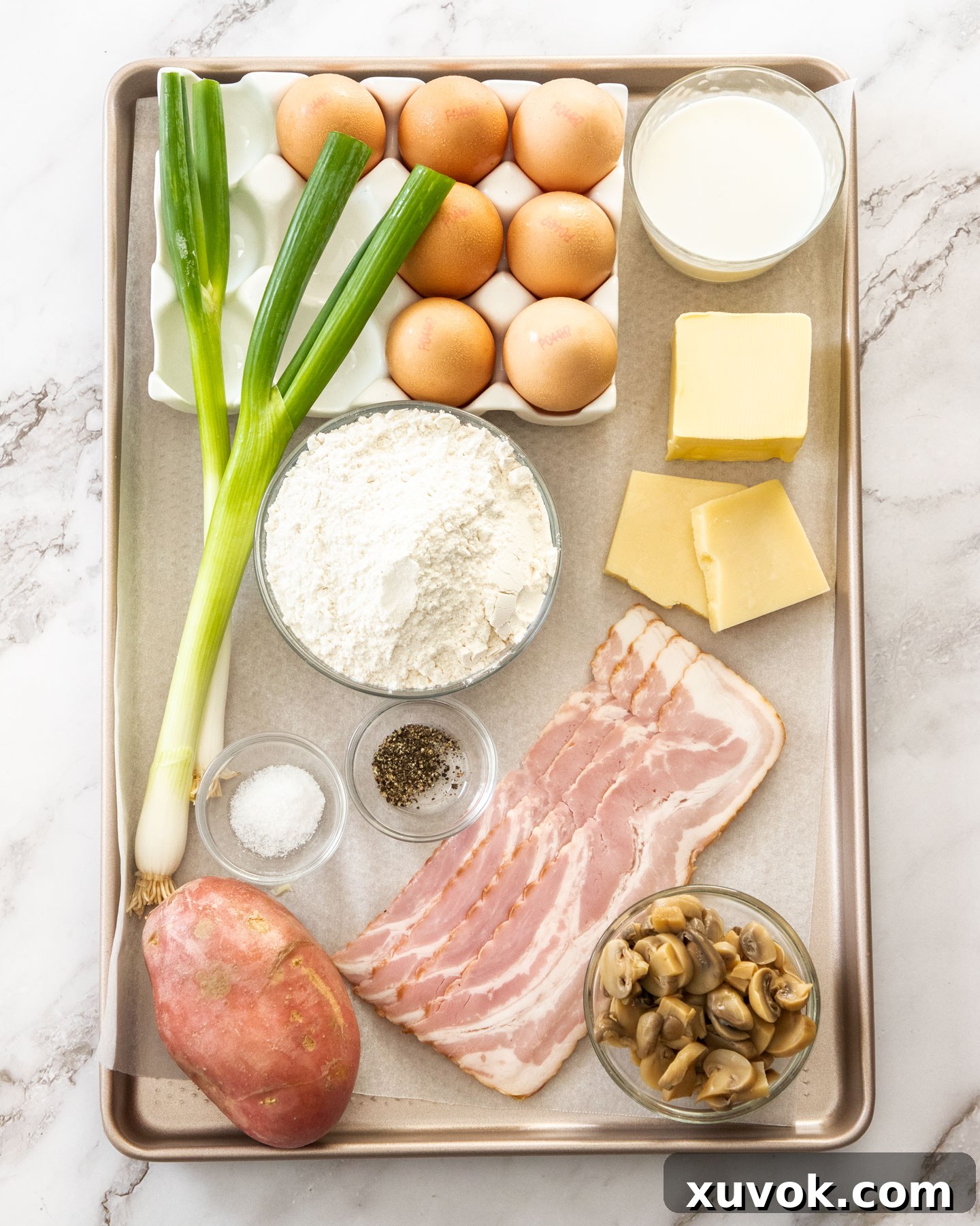 A rustic baking tray displaying all the fresh and prepared ingredients for the bacon and potato quiche, including diced crispy bacon, neatly cubed tender potatoes, vibrant chopped spring onions, finely grated Gruyère cheese, fresh eggs, and earthy mushrooms, all perfectly arranged and ready for assembly.