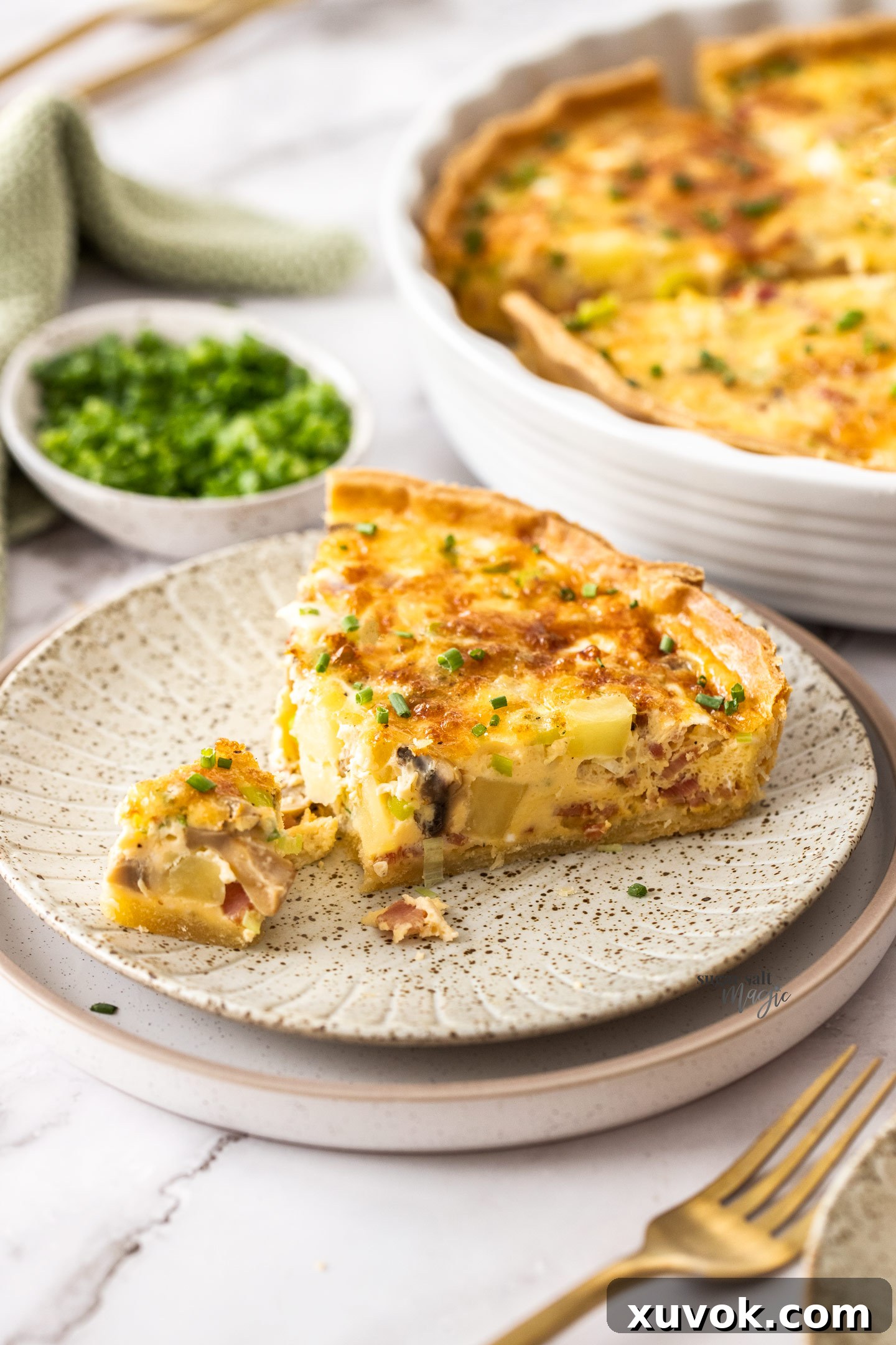 A delectable slice of bacon and potato quiche with a small corner cut out, perfectly showcasing the creamy, cheesy custard and abundant fillings within its golden, flaky crust. Ready to be enjoyed.