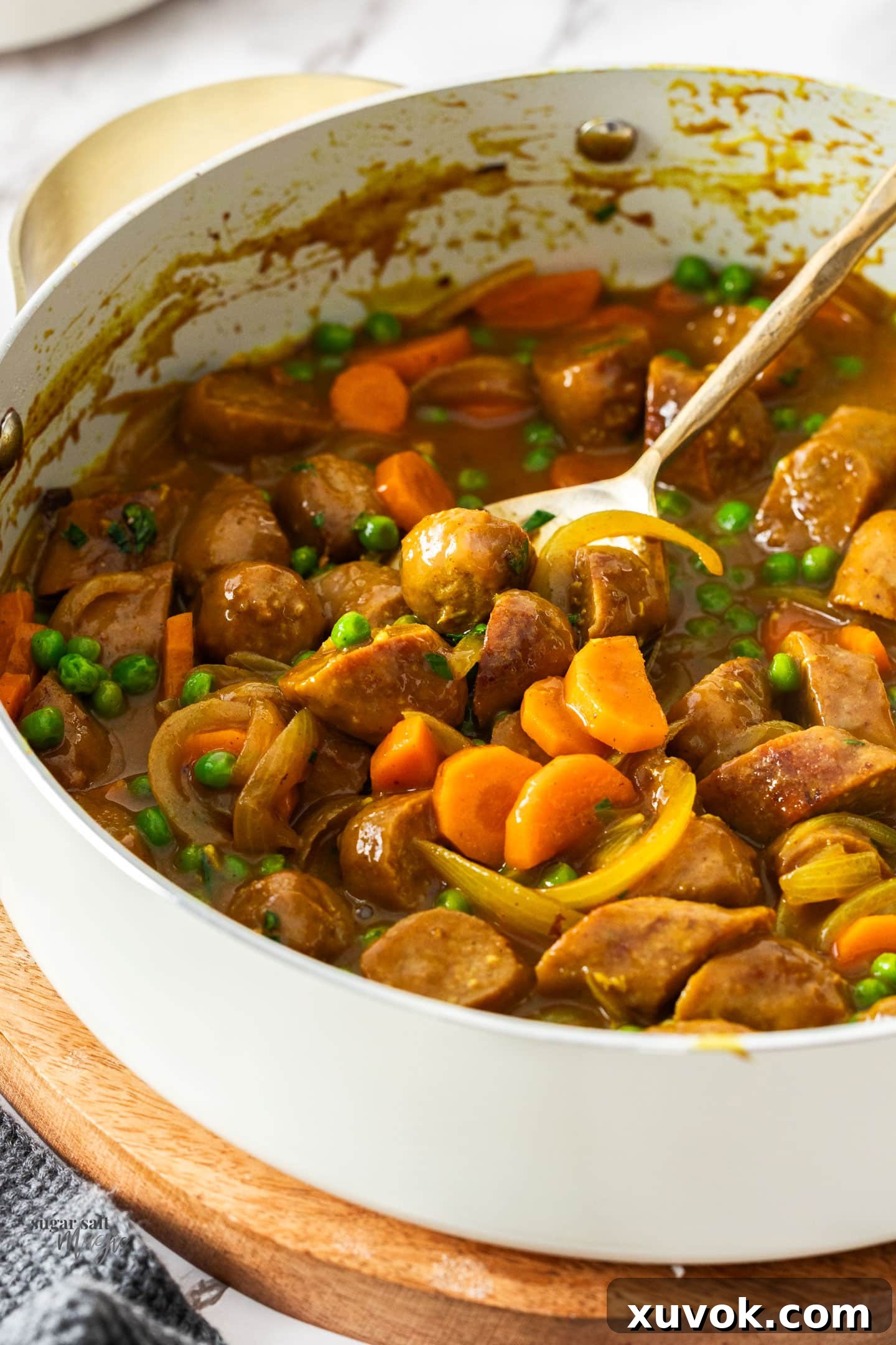 Curried sausages in a pan with a serving spoon.