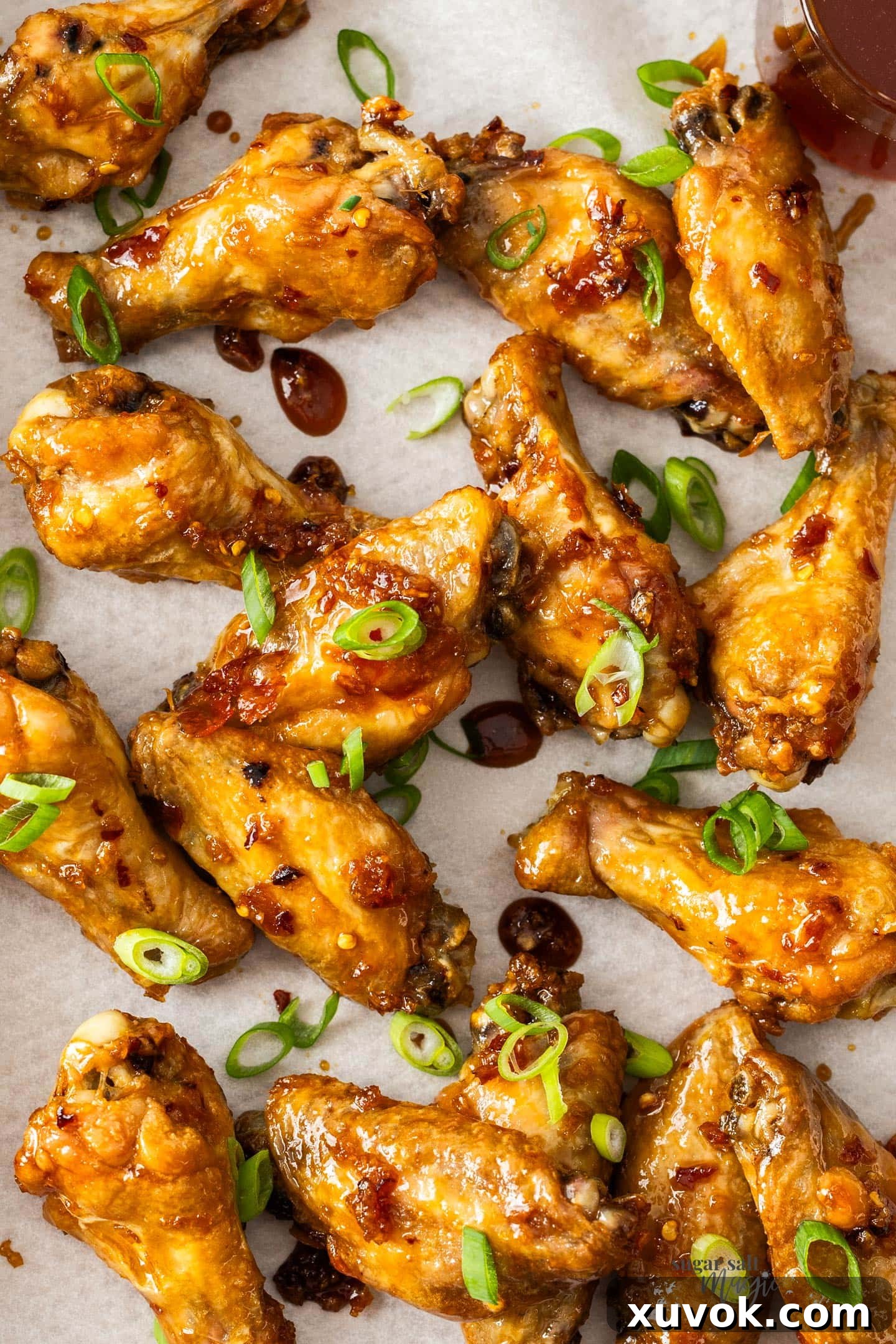Top down view of honey garlic chicken wings on a tray topped with green onions.
