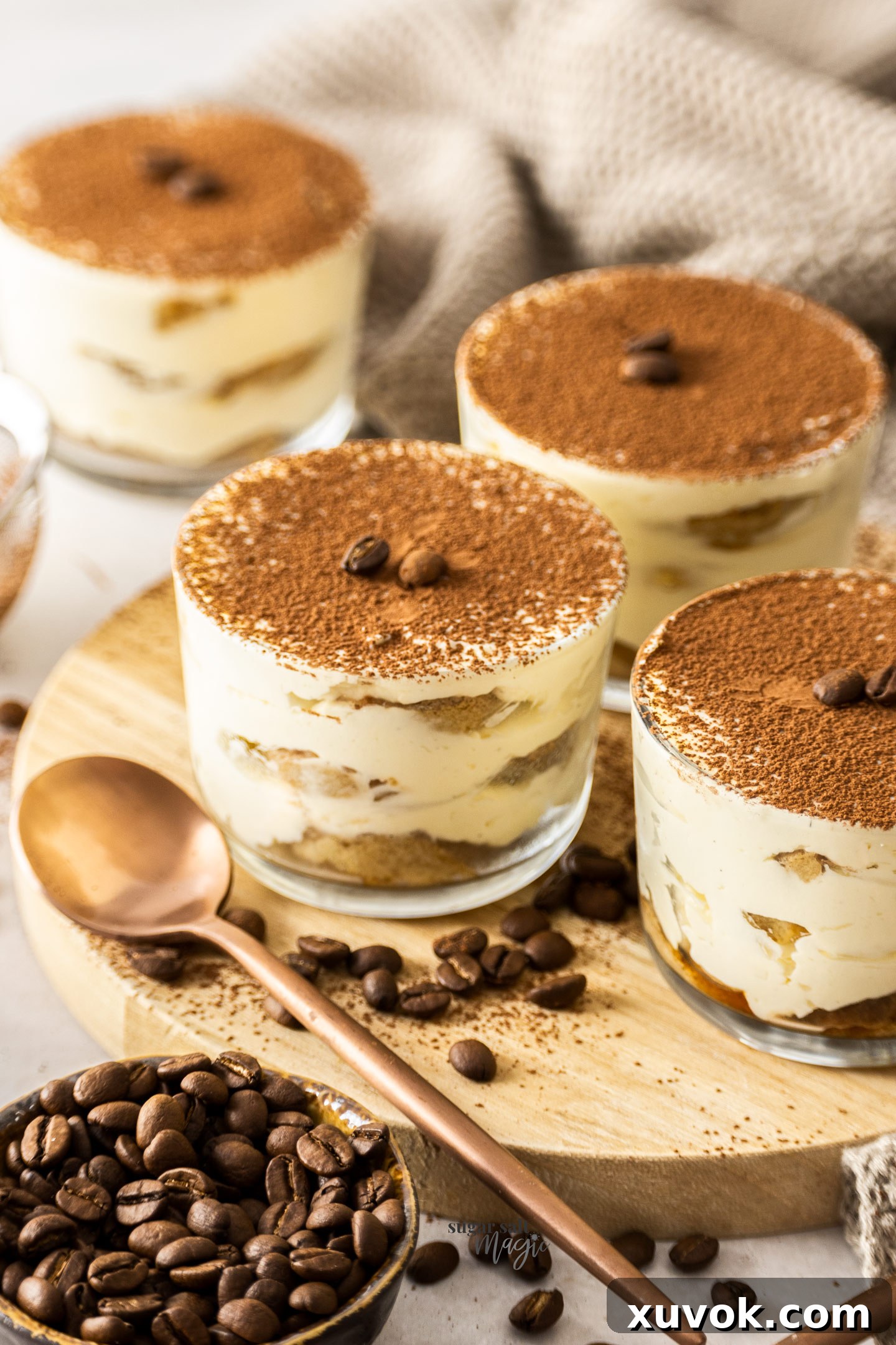 Four individual tiramisu cups perfectly arranged on a rustic wooden platter, showcasing their distinct layers of creamy mascarpone, espresso-soaked ladyfingers, and a dusting of cocoa.
