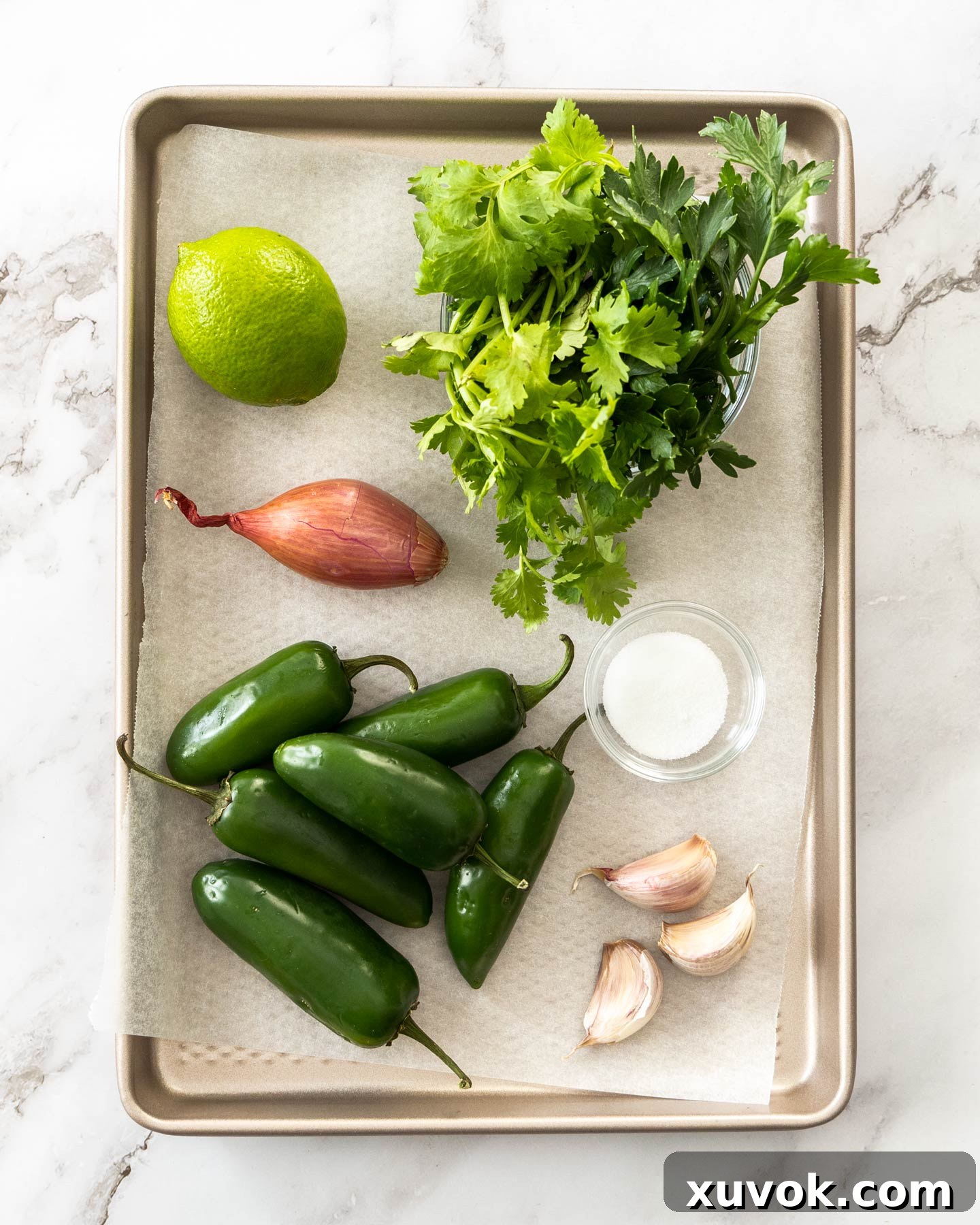 A selection of fresh ingredients including jalapeno peppers, lime, herbs, and shallots laid out on a baking tray, ready for making relish.