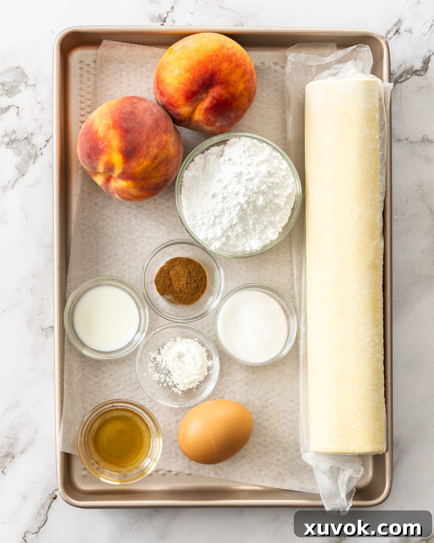 A vibrant selection of ingredients laid out, including fresh peaches, puff pastry, sugars, vanilla, and cinnamon, ready for making peach tarts.