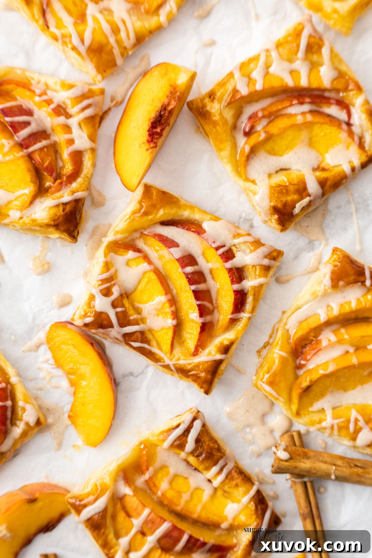 A collection of mini puff pastry peach tarts arranged neatly on a sheet of baking paper, highlighting their golden edges and inviting fillings.
