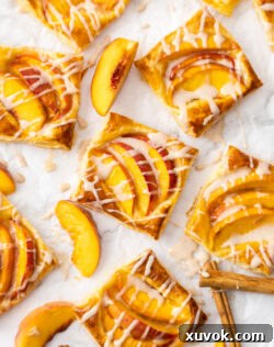 Eight perfectly baked mini puff pastry peach tarts arranged on a sheet of baking paper, ready to be served.
