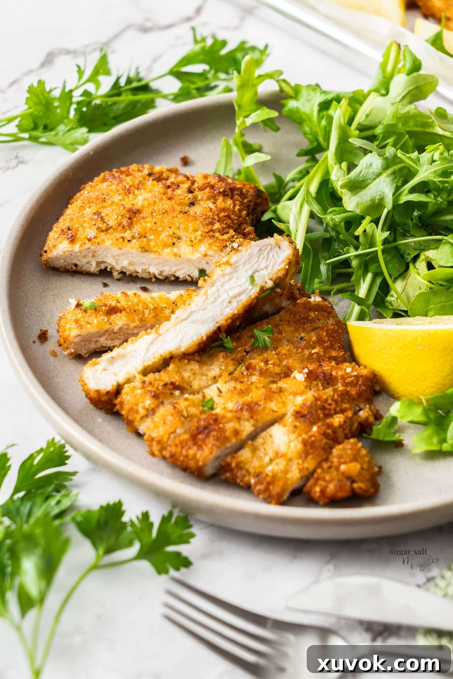 A perfectly cooked Italian chicken cutlet, sliced to reveal its juicy interior, served on a white dinner plate.