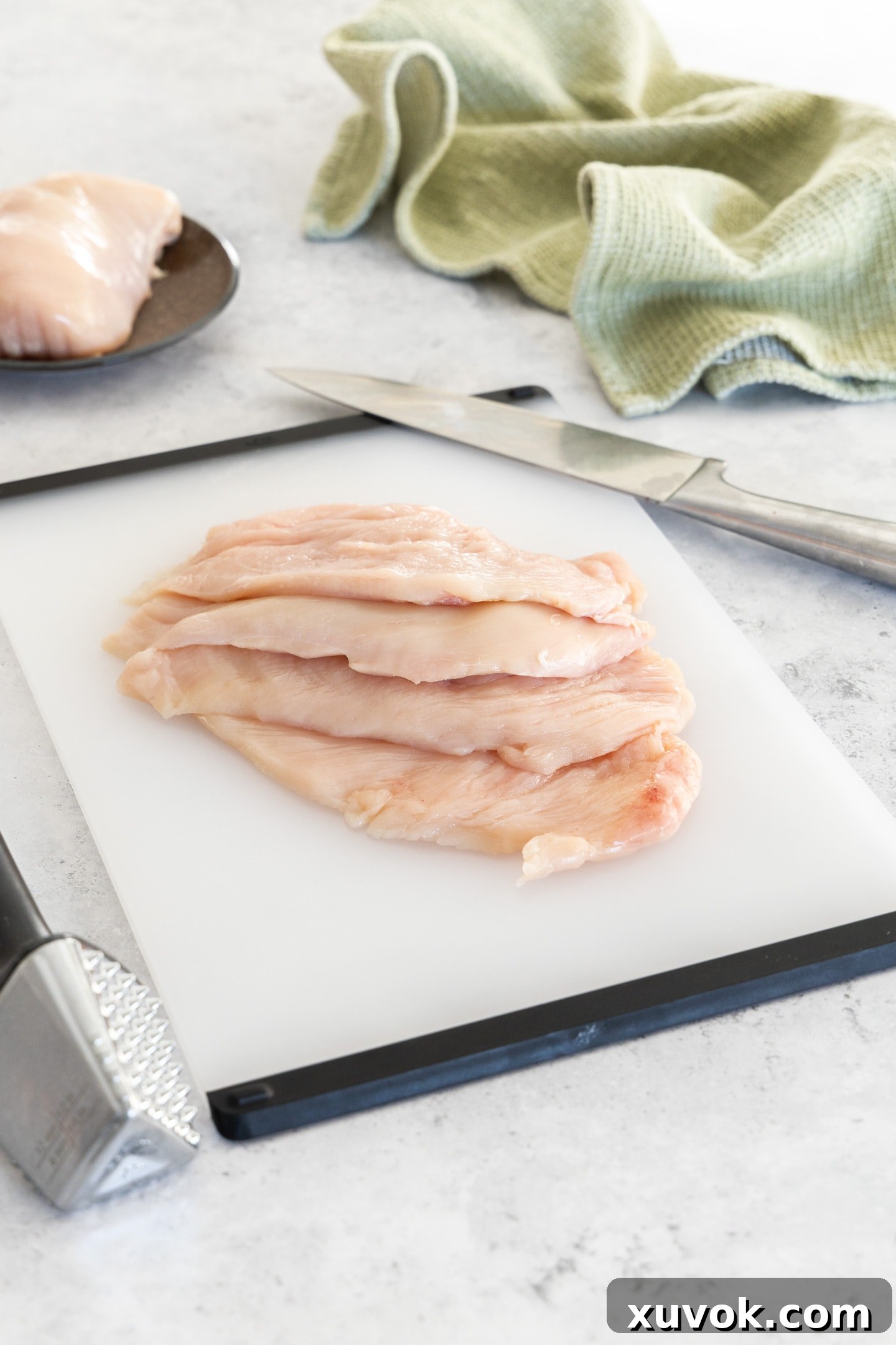 Four perfectly prepared chicken cutlets resting on a clean wooden chopping board, ready for seasoning and cooking. Their uniform thickness promises even cooking.