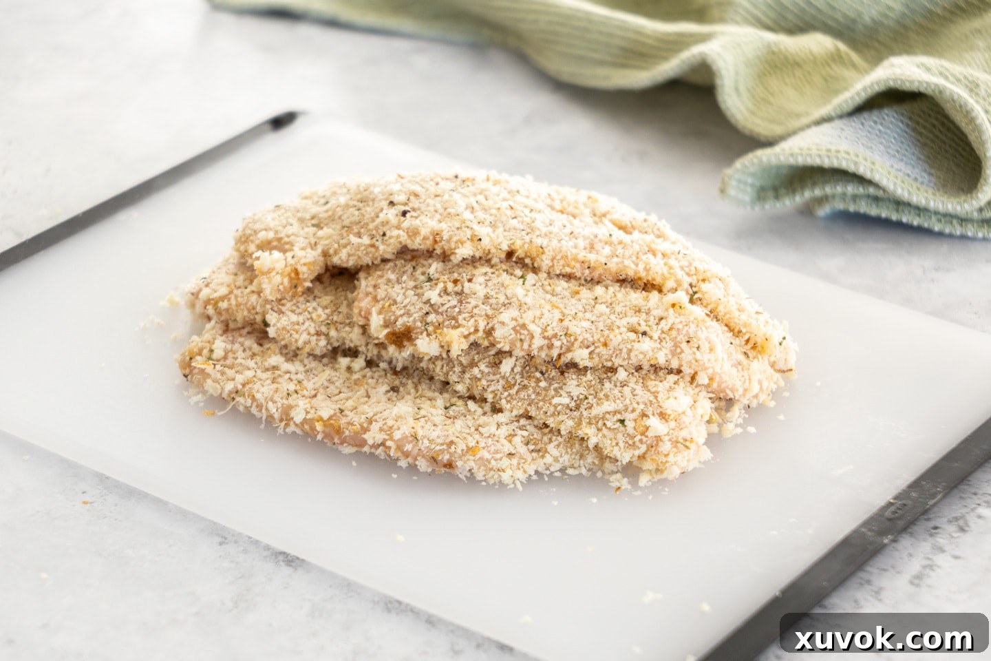 A tray of raw, breaded chicken cutlets neatly arranged on a chopping board, prepared for cooking or future freezing.