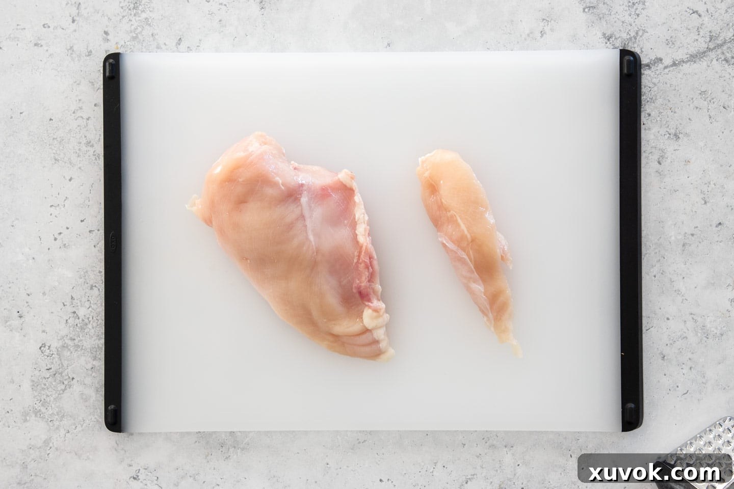 A side-by-side comparison of a full chicken breast fillet and a smaller, distinct chicken tenderloin on a wooden chopping board.