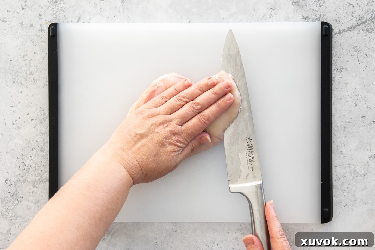 A sharp kitchen knife deftly slicing through a raw chicken breast, illustrating the technique to create two even chicken cutlets.