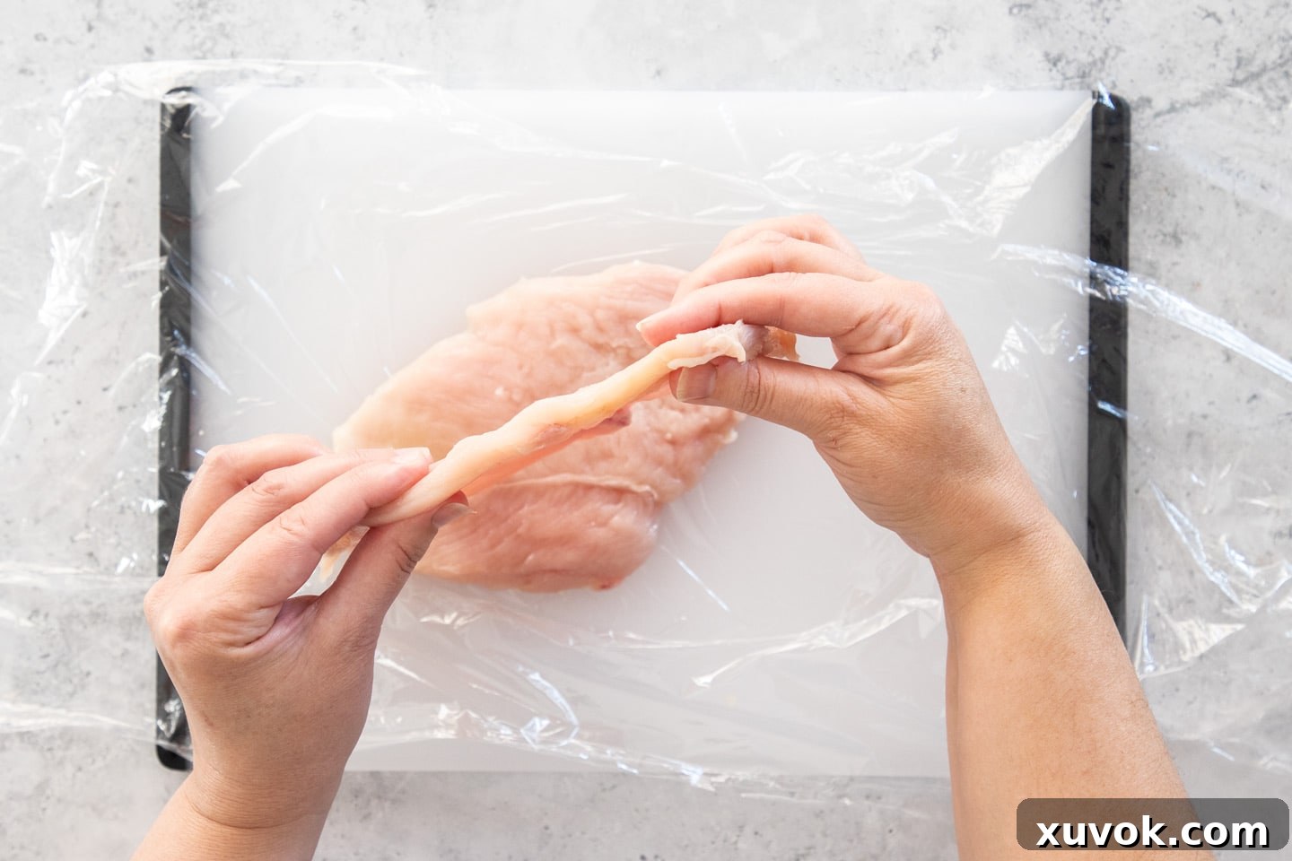 Hands gently holding up a chicken cutlet to reveal its consistent and ideal thickness of approximately ¼ inch (6-7mm).