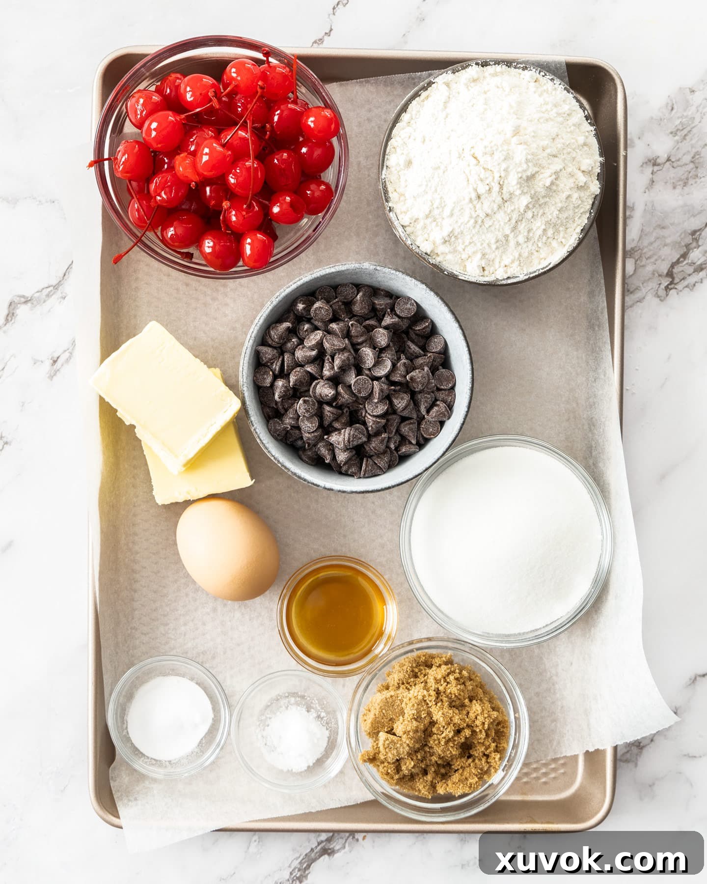 Ingredients for the cherry chocolate chip cookies laid out on a baking tray including cherries, chocolate chips, butter, flour, and sugar.