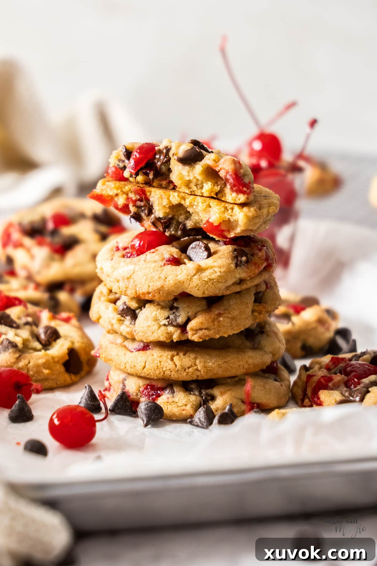 A stack of cherry chocolate chip cookies with the top one broken in half to show its soft, chewy interior with melted chocolate and cherry pieces.