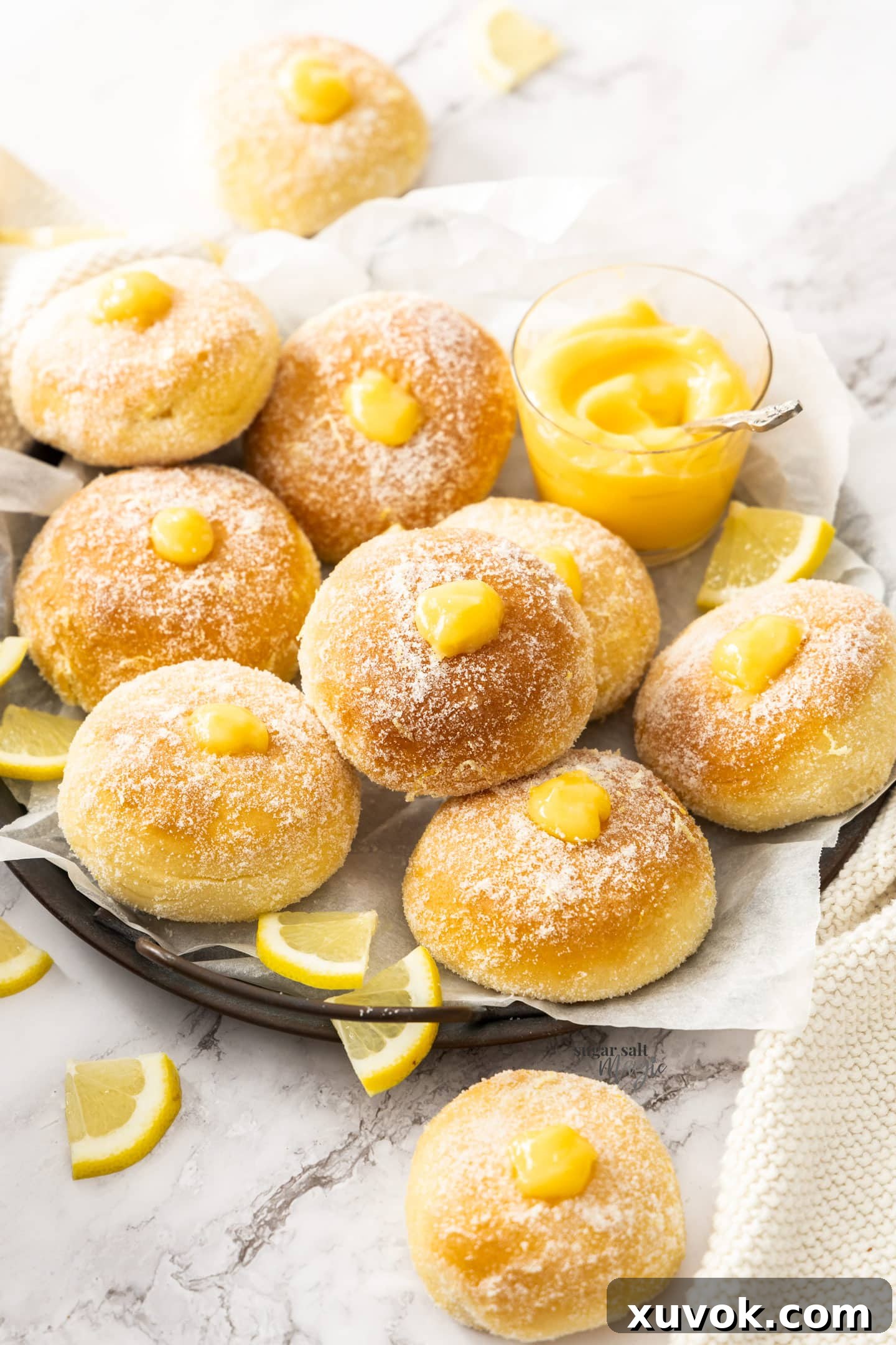 A dark tray with 10 fluffy lemon filled donuts, generously coated in lemon sugar and bursting with vibrant lemon curd.