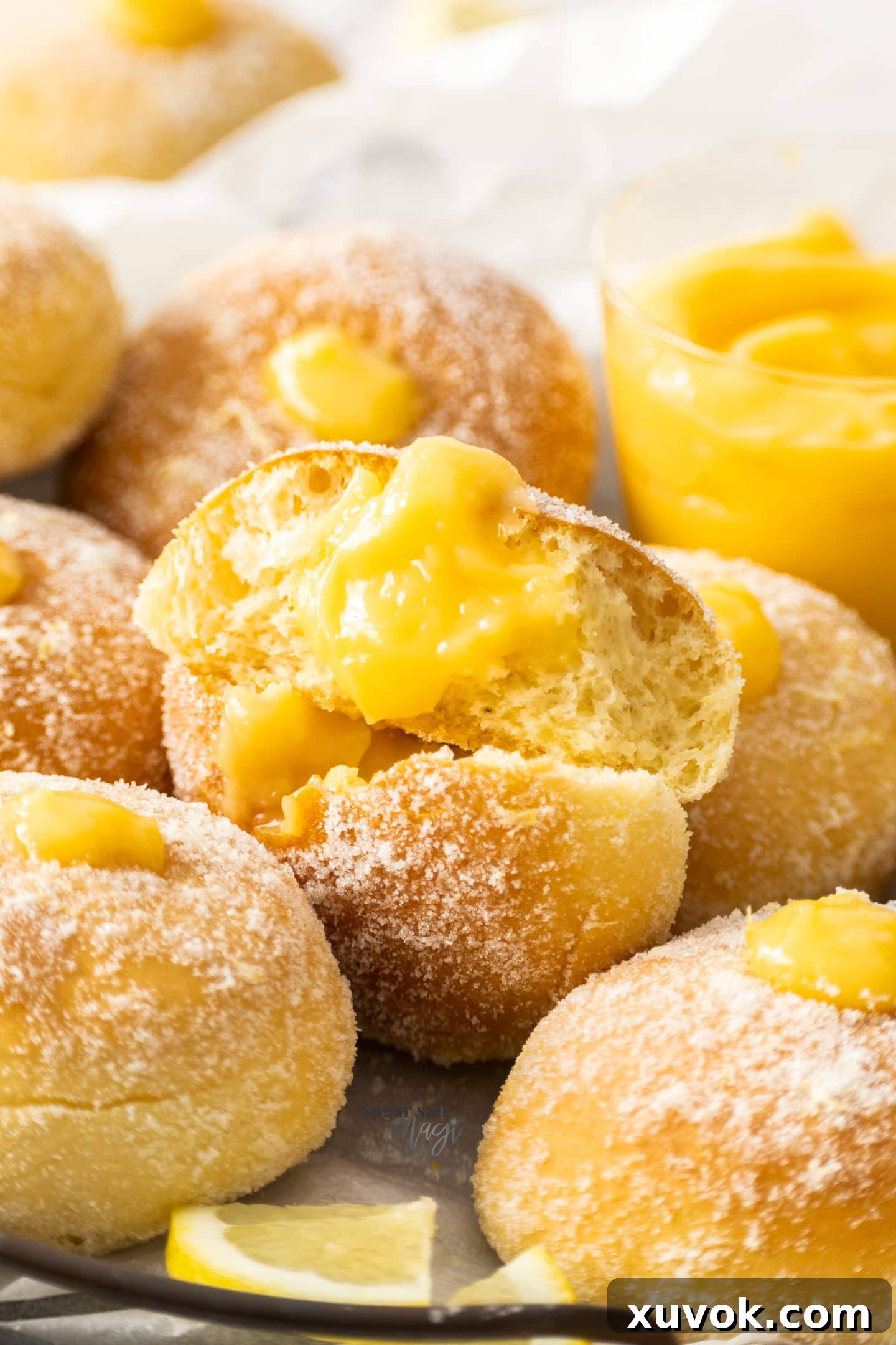 A baked lemon donut broken in half, revealing the fluffy interior and the generous, vibrant lemon curd filling.