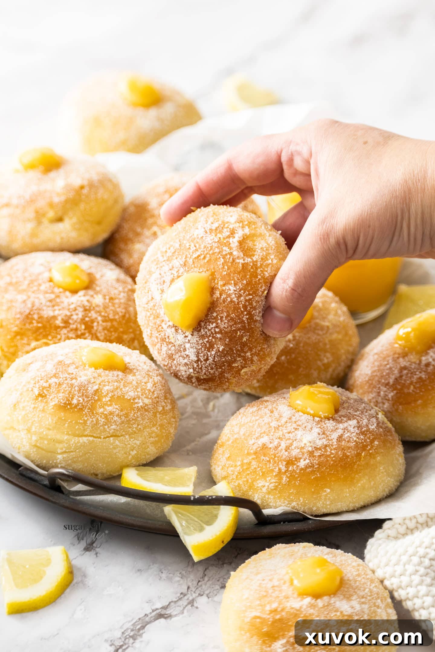 A hand reaching for and holding a perfectly baked lemon donut, coated in lemon sugar, with a hint of lemon curd peeking out.