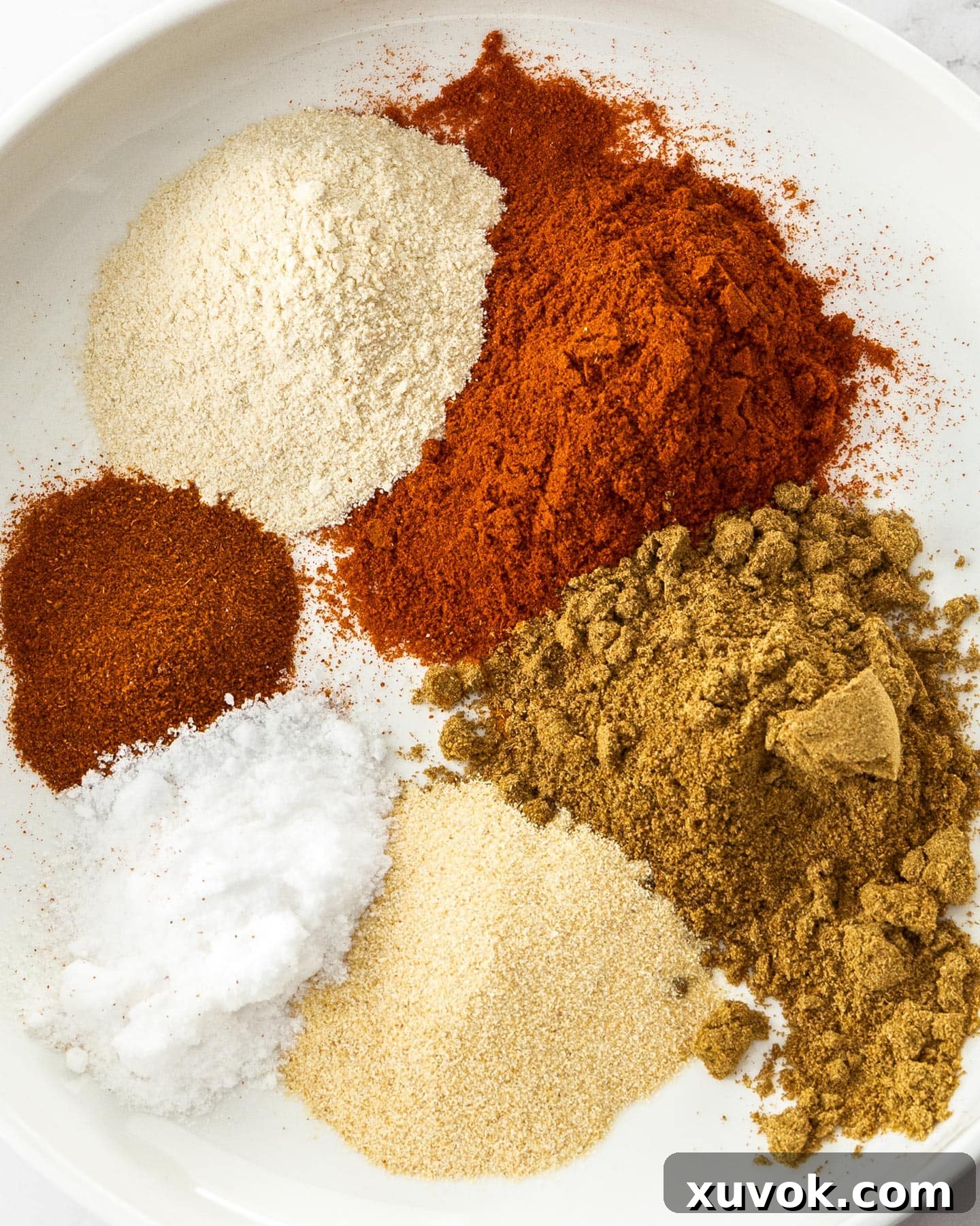 Different spices in piles on a plate, including paprika, cumin, and chili powder, ready for mixing into fajita seasoning.