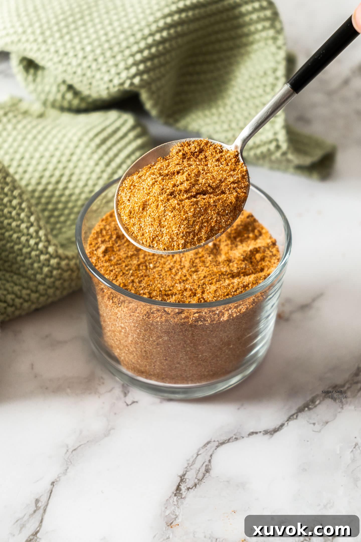 A spoon taking fajita seasoning from a glass jar, showcasing the rich color of the blend.