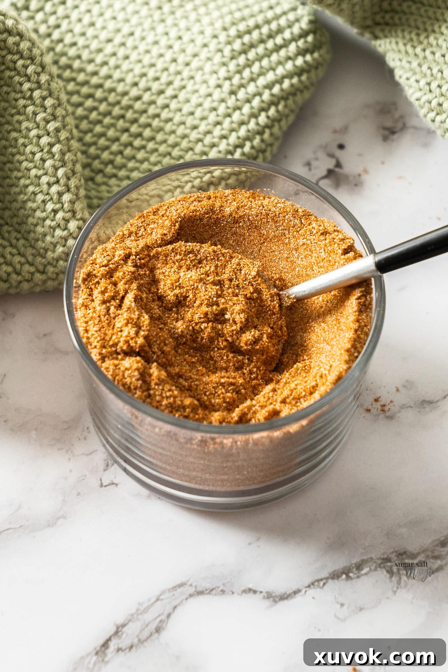 A glass full of fajita seasoning with a spoon resting in it, ready for use in cooking.