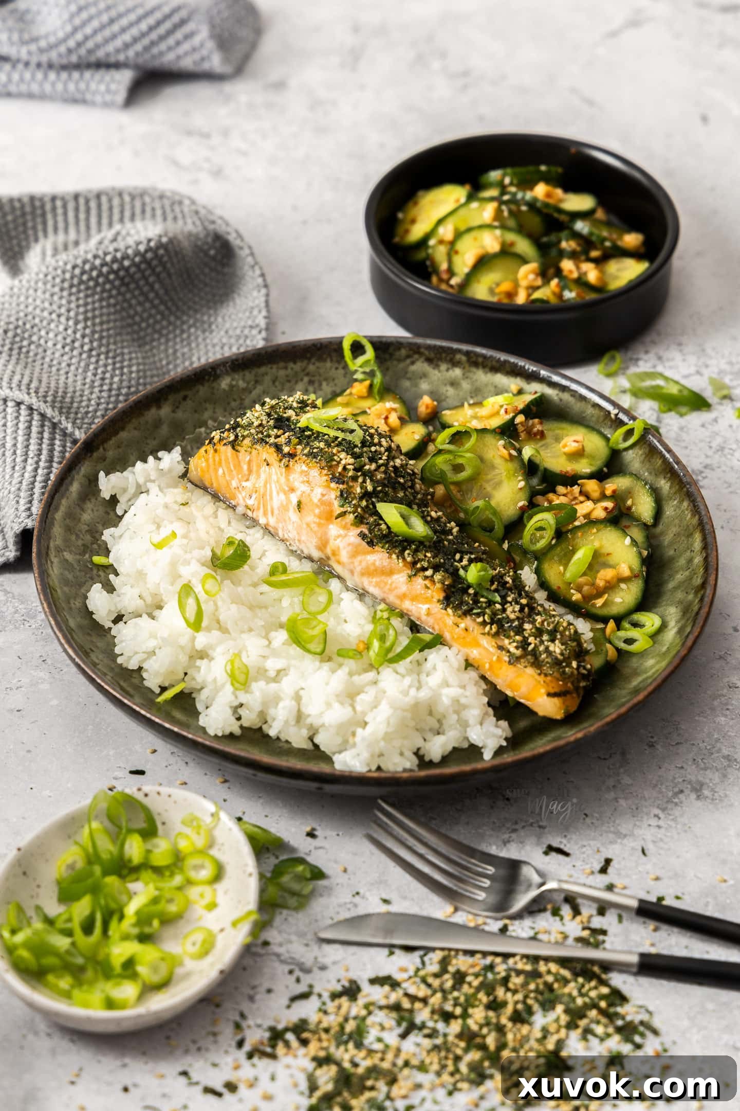 A perfectly cooked furikake salmon fillet resting on a bed of steamed rice, accompanied by a fresh cucumber salad.