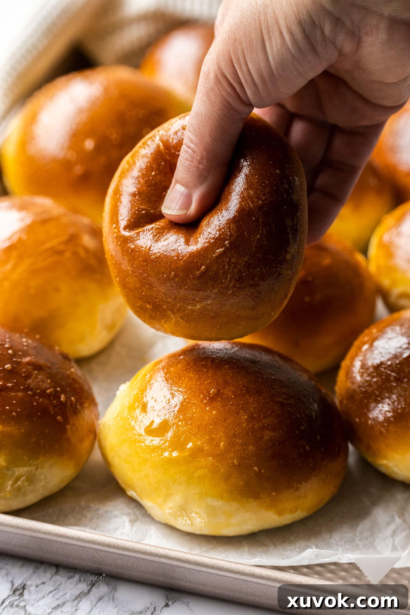 A hand gently presses down on a freshly baked maritozzo bun, illustrating its incredible softness and fluffy, airy texture. This image highlights the desired quality of the bun before filling.