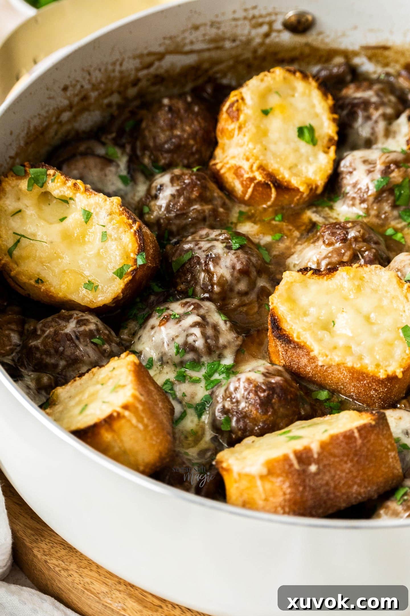 Close-up of French onion meatballs in a pan, smothered in rich gravy and generously topped with melted, bubbly Gruyere cheese.