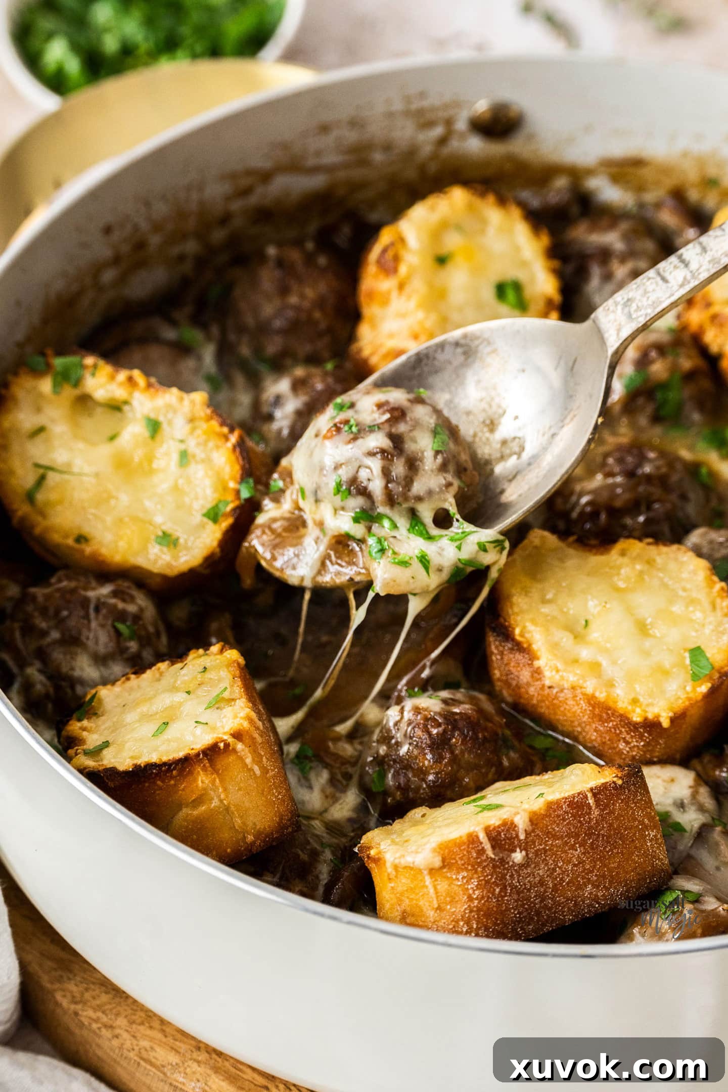 A spoon gently lifts a tender French onion meatball from the pan, coated in rich gravy and melted cheese.