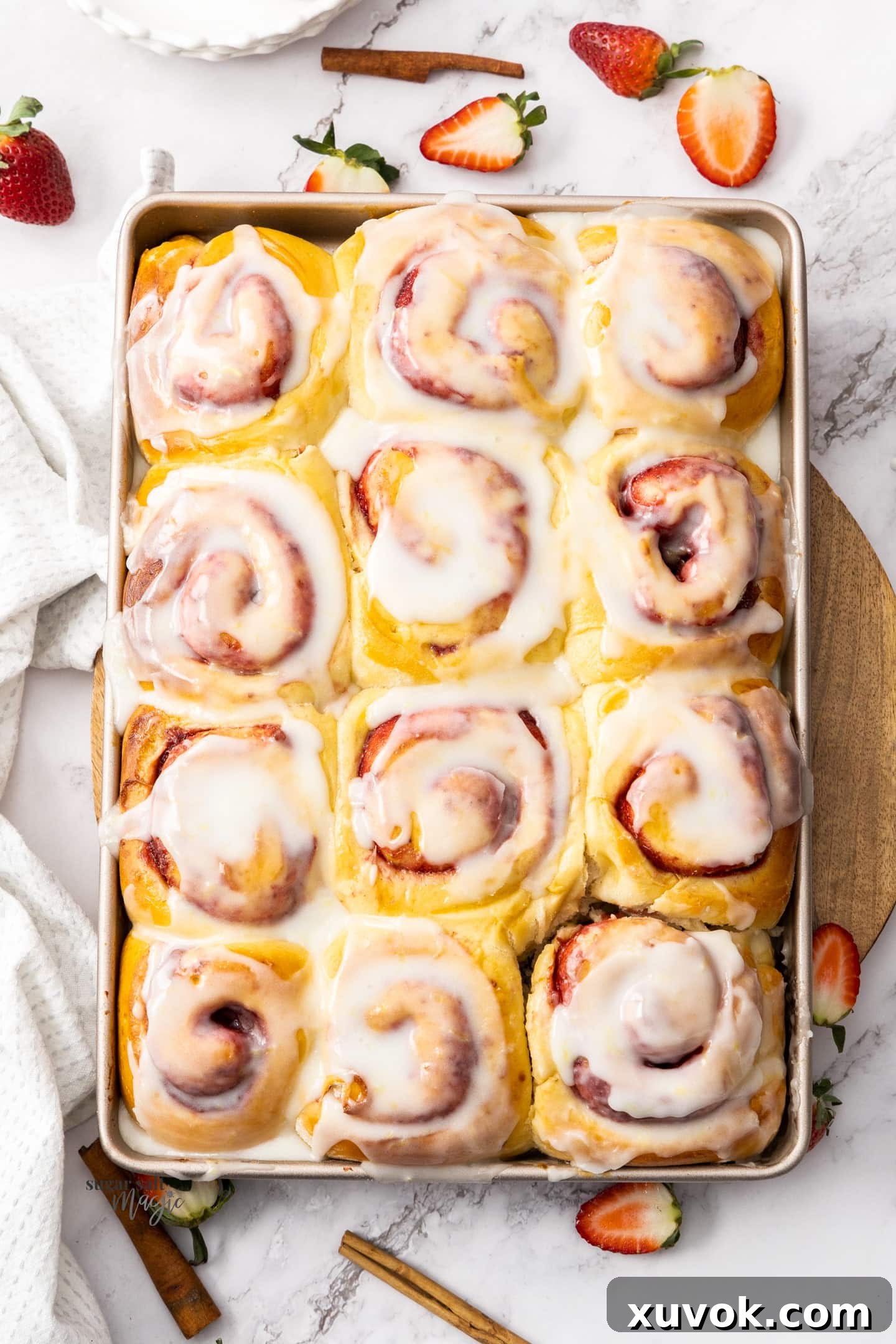 Twelve golden-brown strawberry cinnamon rolls, generously drizzled with lemon glaze, arranged in a rectangular baking pan.