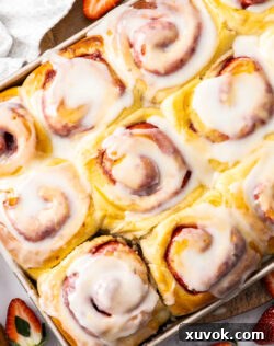A batch of strawberry cinnamon rolls generously covered with white lemon glaze in a baking pan.