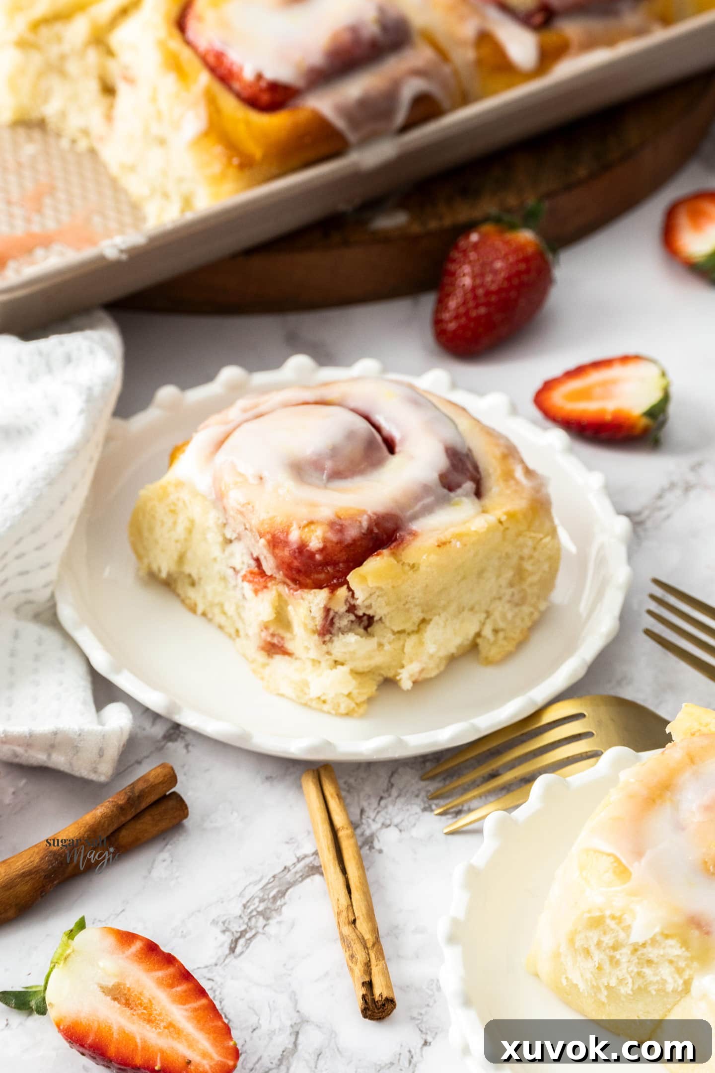 A single strawberry cinnamon roll, beautifully glazed, presented on a white dessert plate, showing its soft interior and luscious filling.