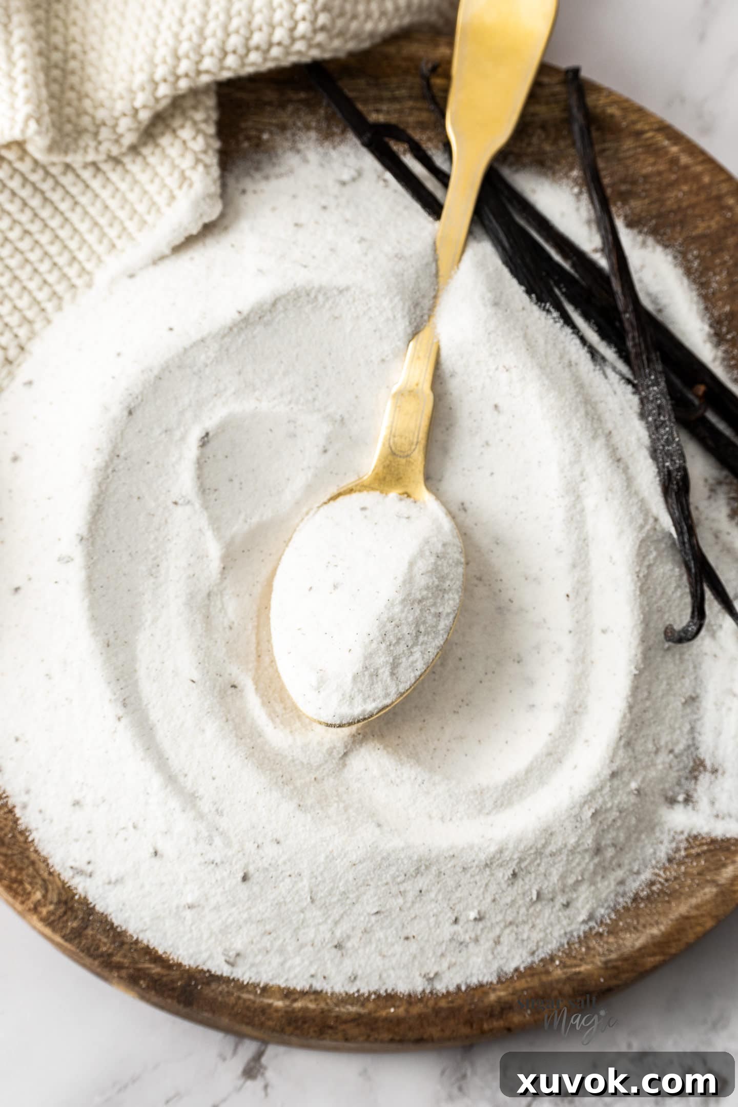 A spoon of homemade vanilla sugar on top of a pile of it, showcasing its rich texture and vanilla specks.
