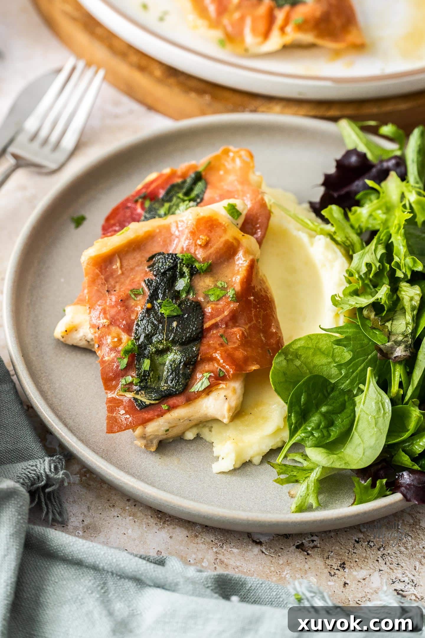 Two generous pieces of chicken saltimbocca, perfectly cooked and coated in sauce, elegantly plated on a bed of fluffy mashed potatoes, garnished with fresh herbs.